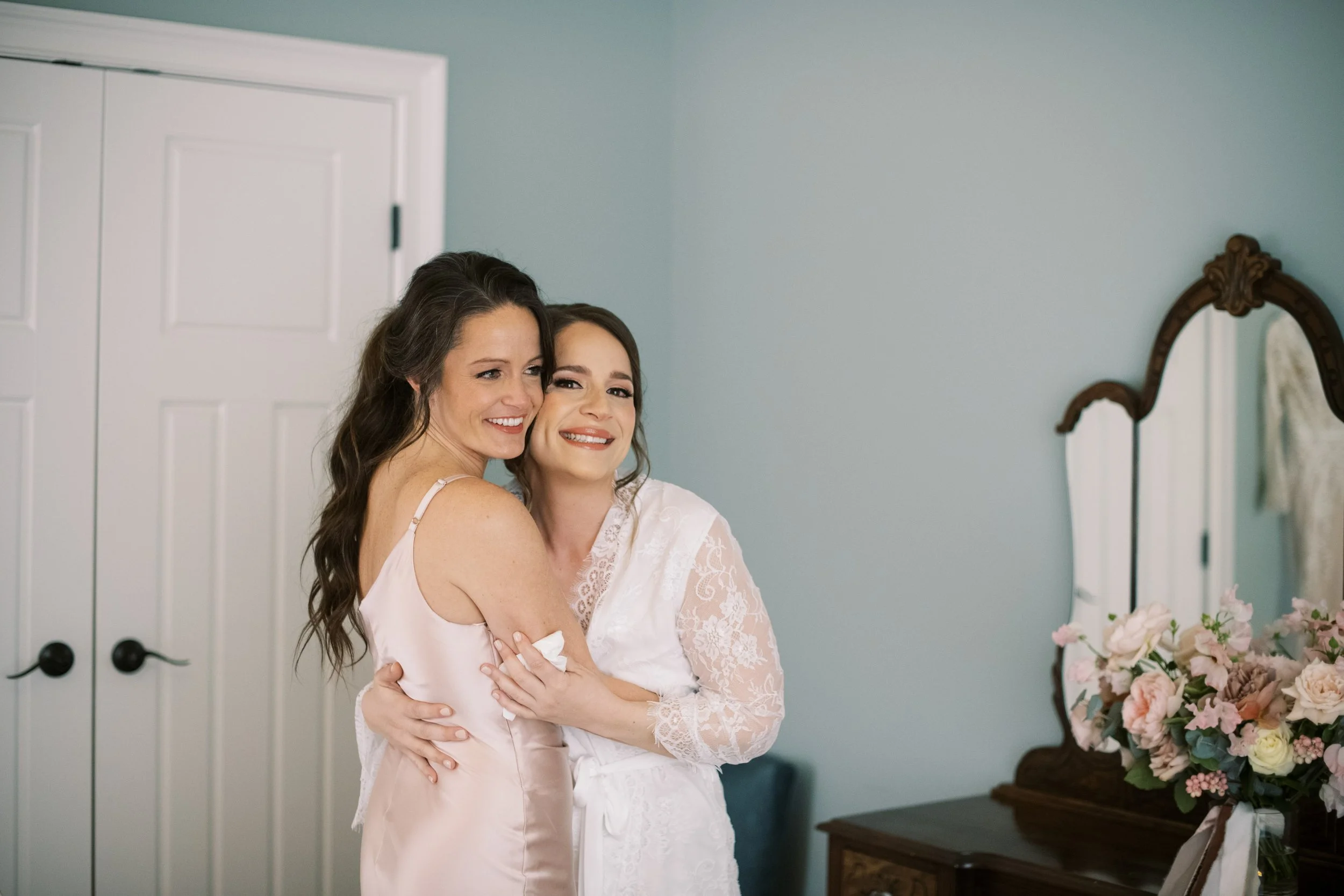 The bride embraces her maid of honor during a quiet getting ready moment, sharing a heartfelt hug in a softly lit room before the wedding day begins at The Bradford.