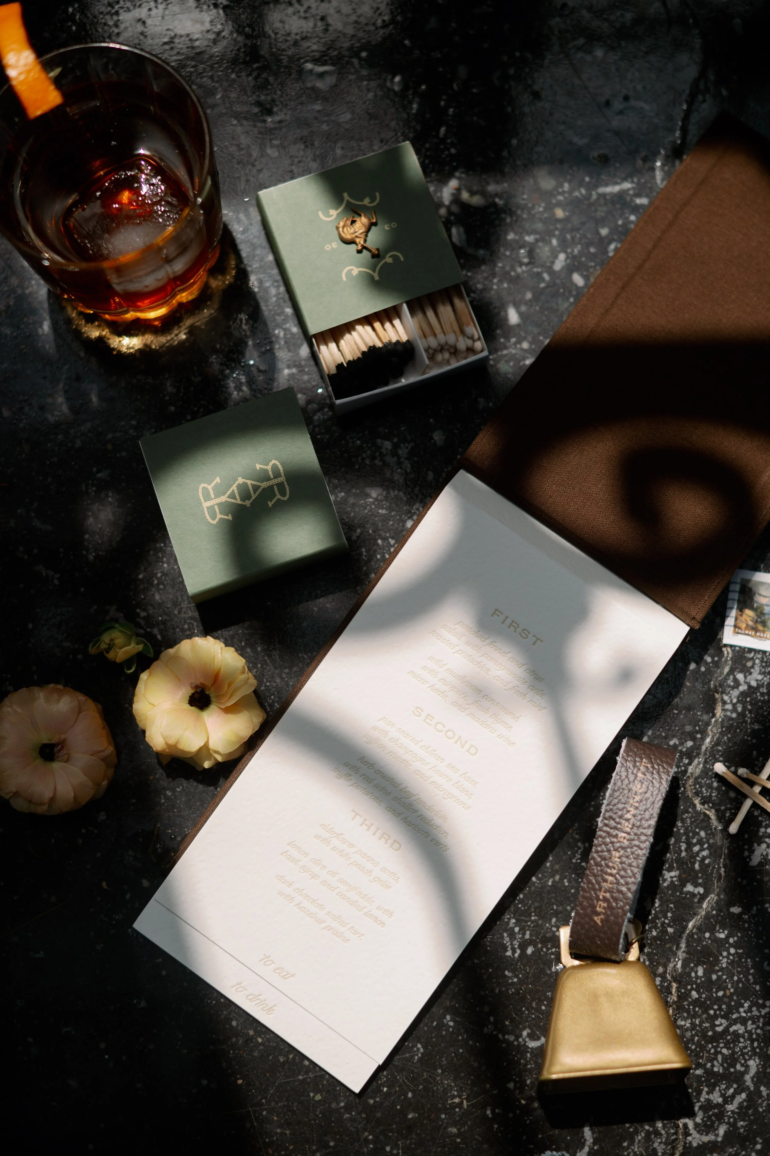 Wedding day flat lay details including invitation suite, matchbook, and whiskey glass at North Carolina wedding