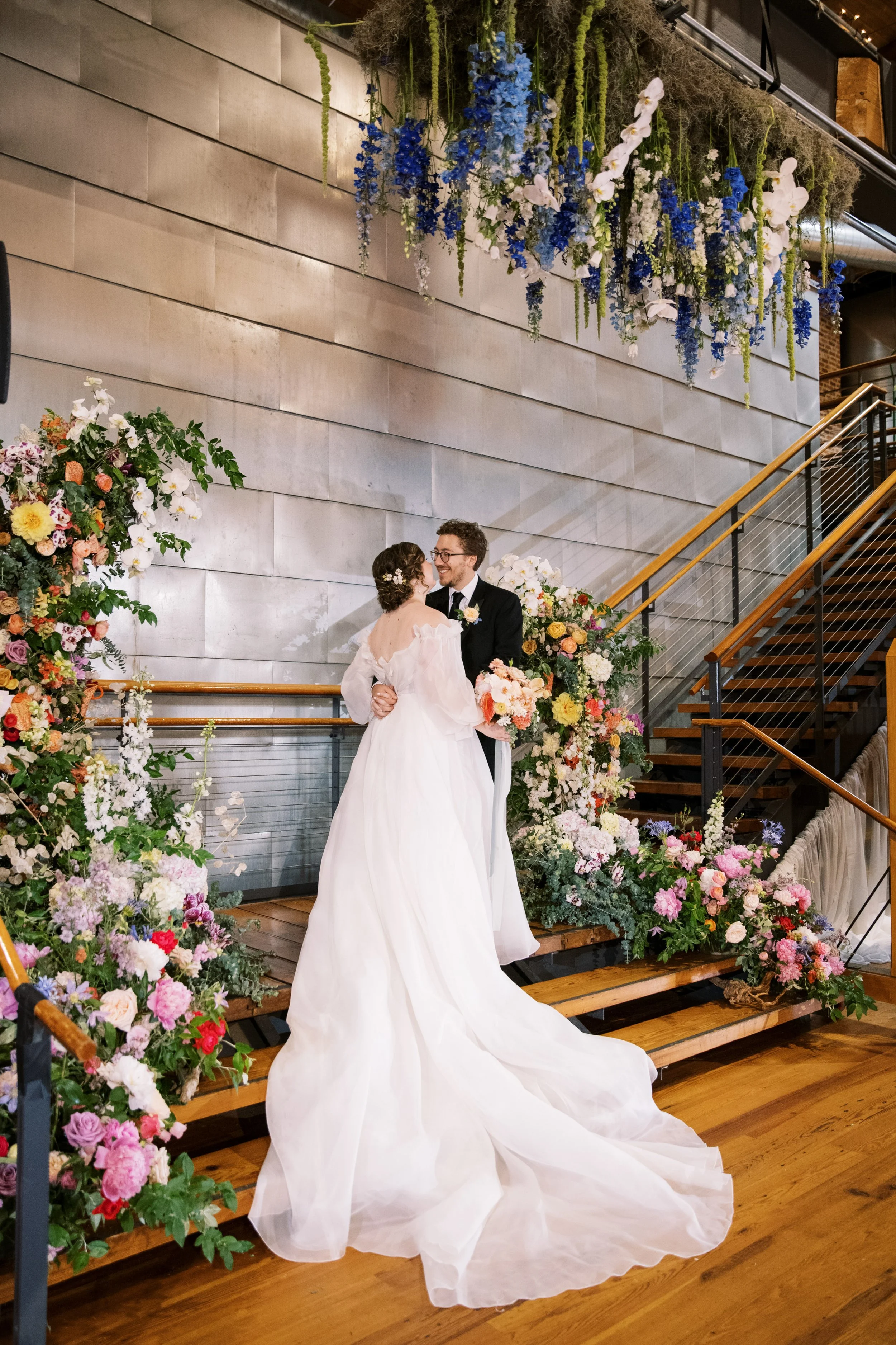 Bride and groom standing on a flower-lined staircase during their Bay 7 wedding ceremony at American Tobacco Campus in Durham, North Carolina.