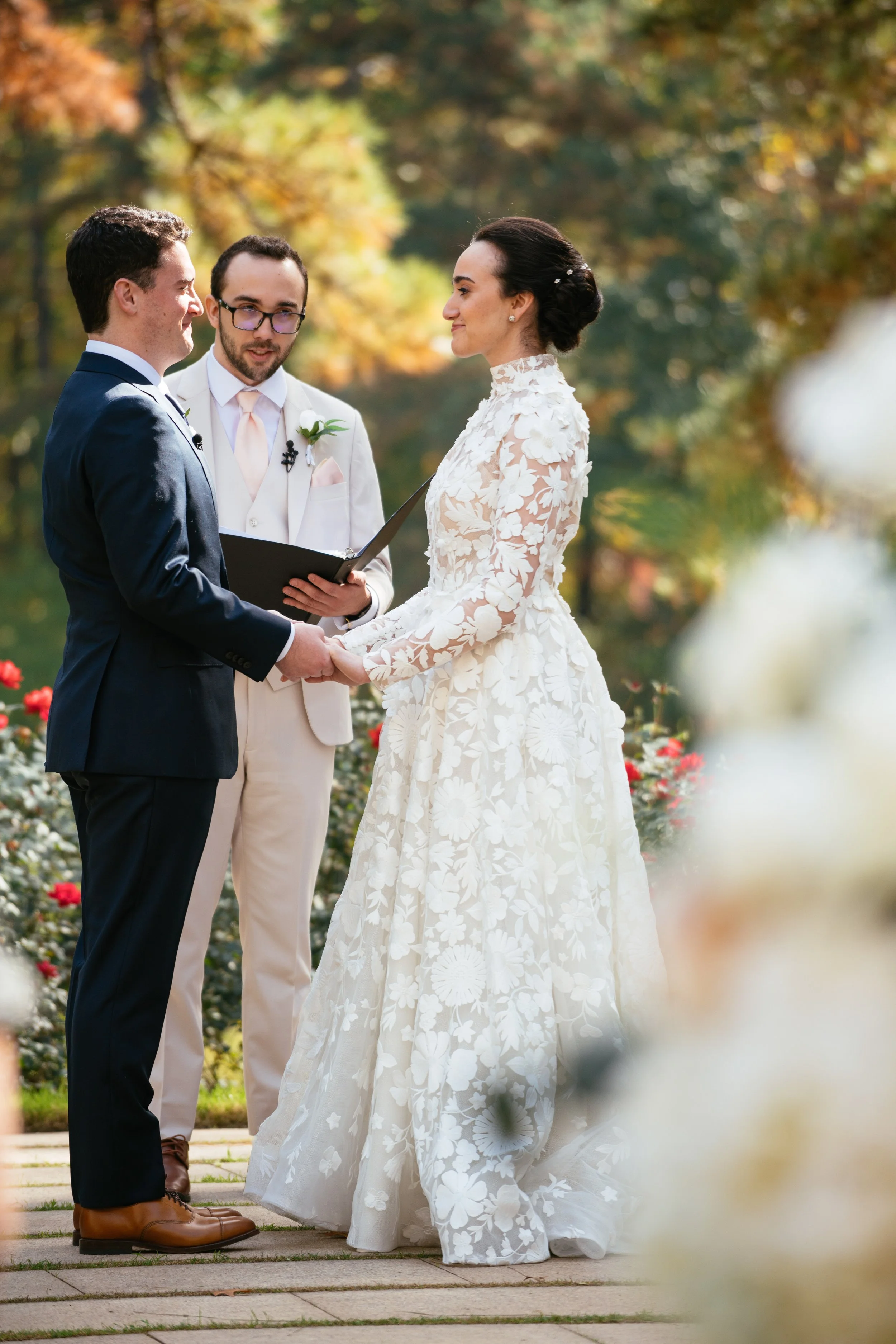 Claudia and Kyle exchange vows during their outdoor wedding ceremony at The Umstead Hotel in Cary North Carolina surrounded by fall foliage and family