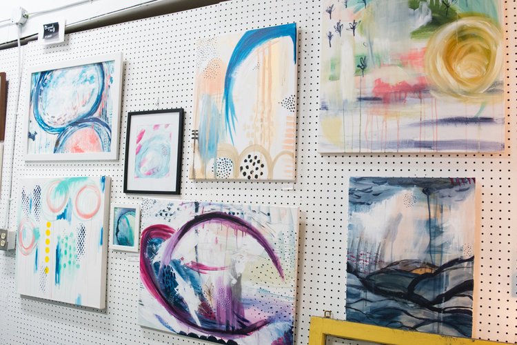  Jaci's studio wall filled with various abstract paintings.&nbsp; 