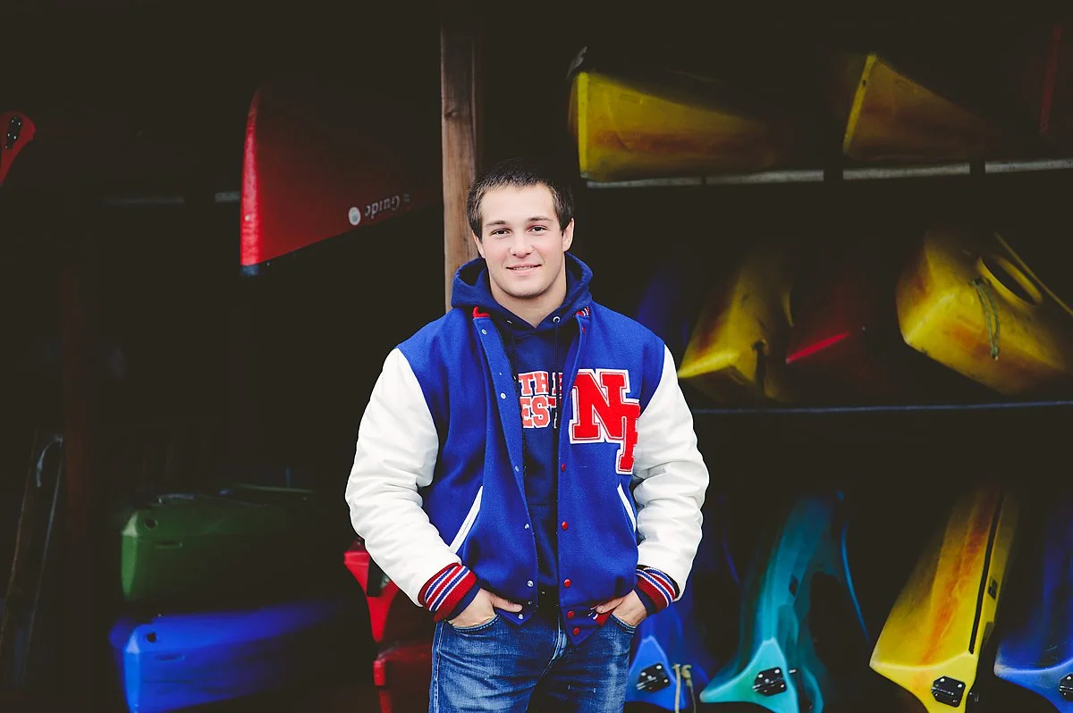 Senior Boy in Lettermen's Jacket, colorful photo with canoes, a vibrant Senior Experience Photoshoot. 
