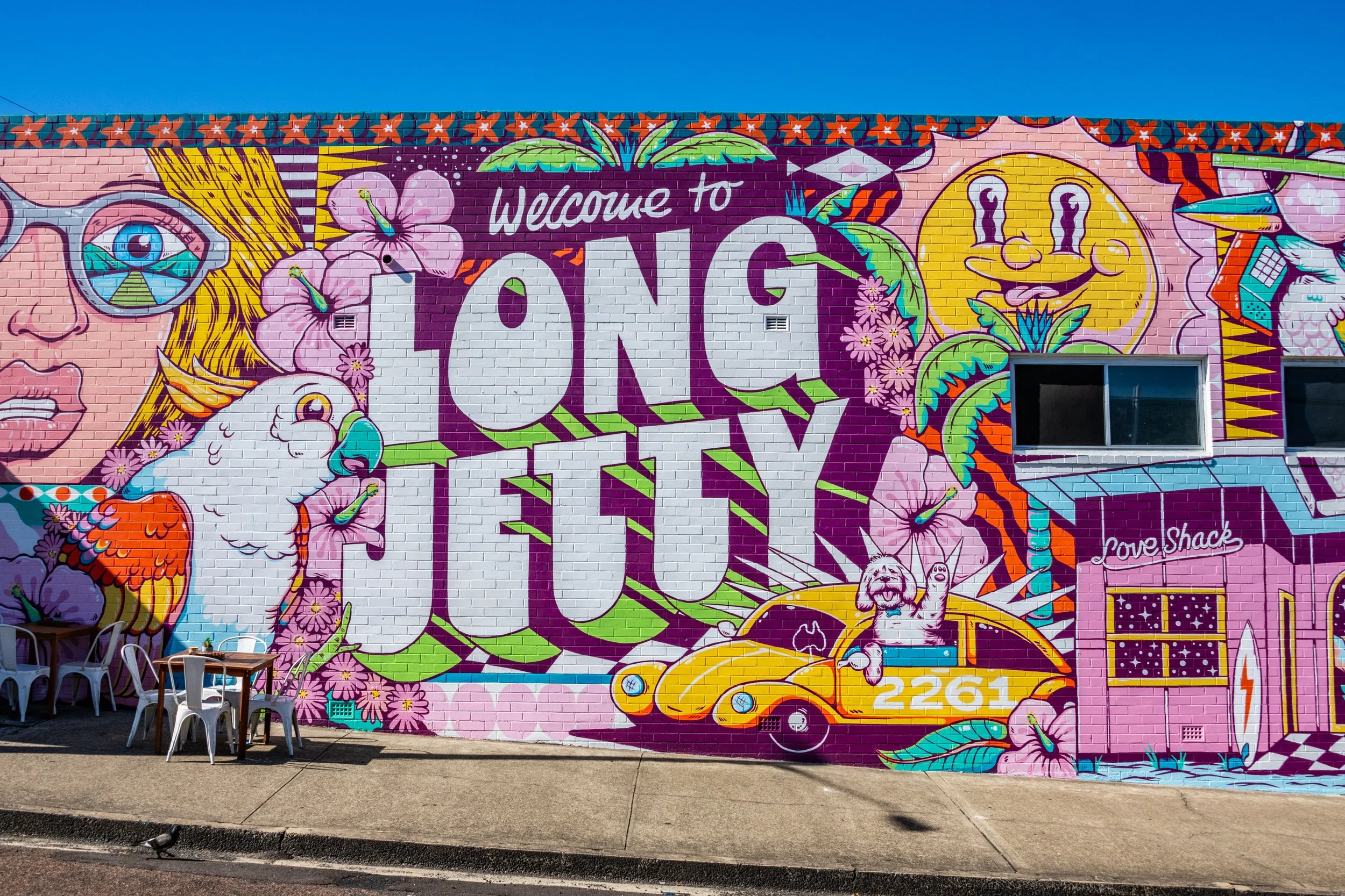 The vibrant colors of the Long Jetty mural bring the seaside community to life, capturing the essence of coastal charm and artistic expression. Rich blues and turquoise hues evoke the nearby ocean, while bright yellows and oranges symbolize the war