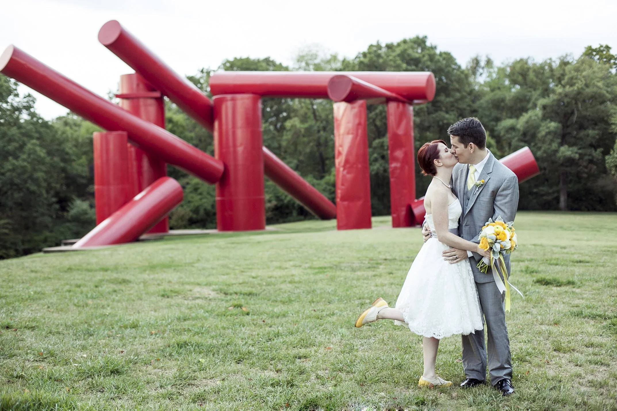 Couple in wedding attire kiss in front of sculpture at Laumeier Sculpture Park.