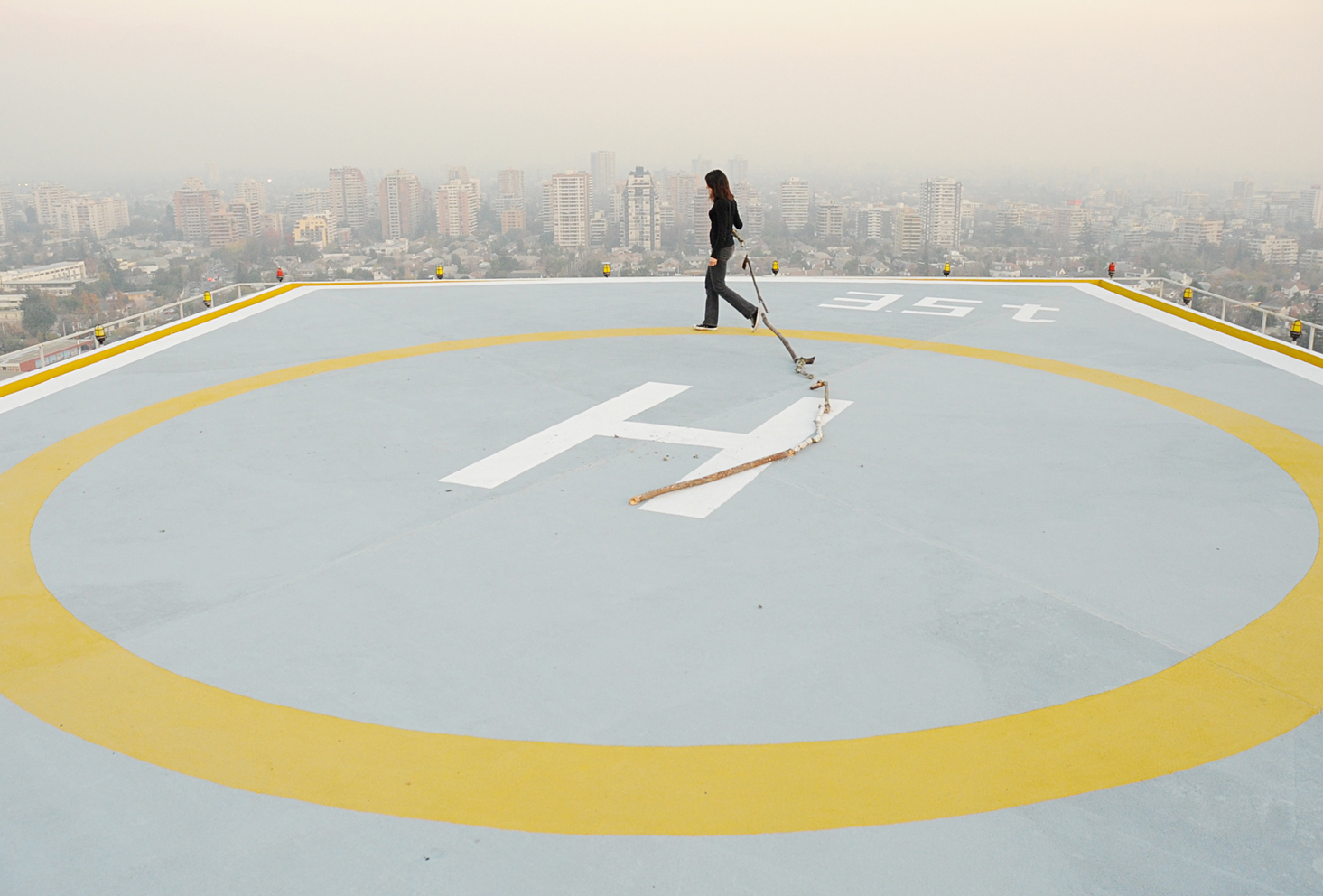 Helipuerto, girando con los palos. 2010. Fotografía de la serie de performance de caminatas con los palos: Caminatas, el cuerpo y la prótesis, 2010-2014. Impresión Lambda. 80 x 120 cm. Heliport, turning with the sticks, 2010. From the series of performance with the sticks: Walks, The Body and the Prosthetic, 2010-2014. Lambda print, 80 x 120 cm.
