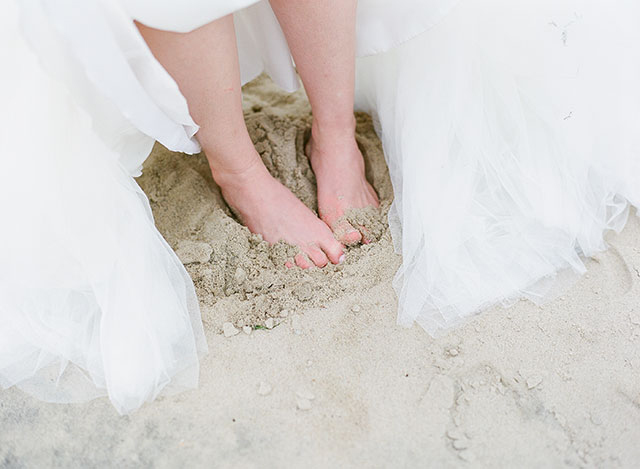 bride takes off shoes for portraits on the beach