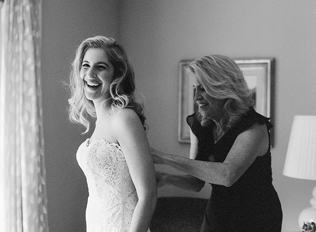 film black and white photo of bride putting on dress with mother