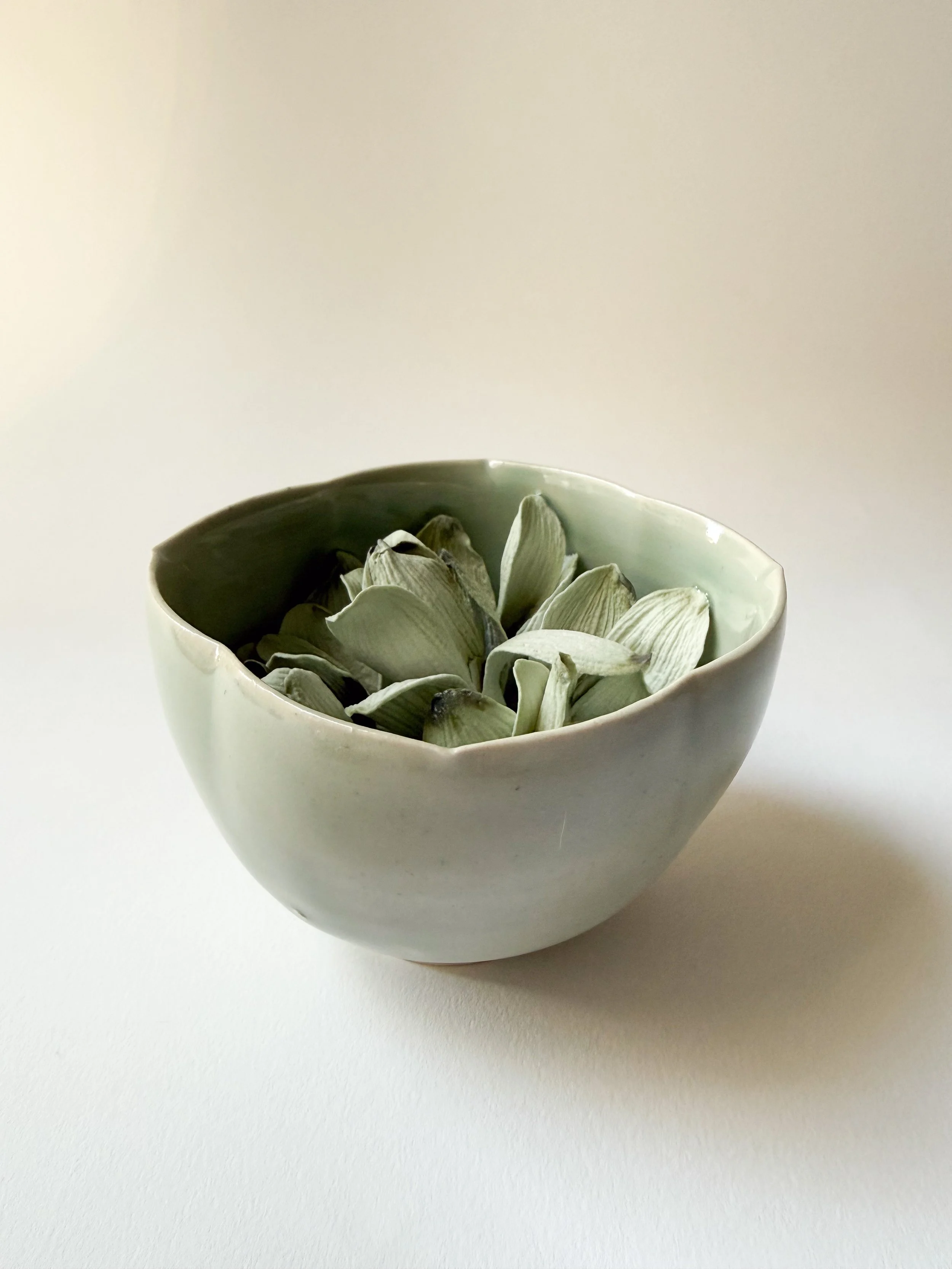 Ceramic bowl filled with porcelain magnolia petals on a plain white surface.
