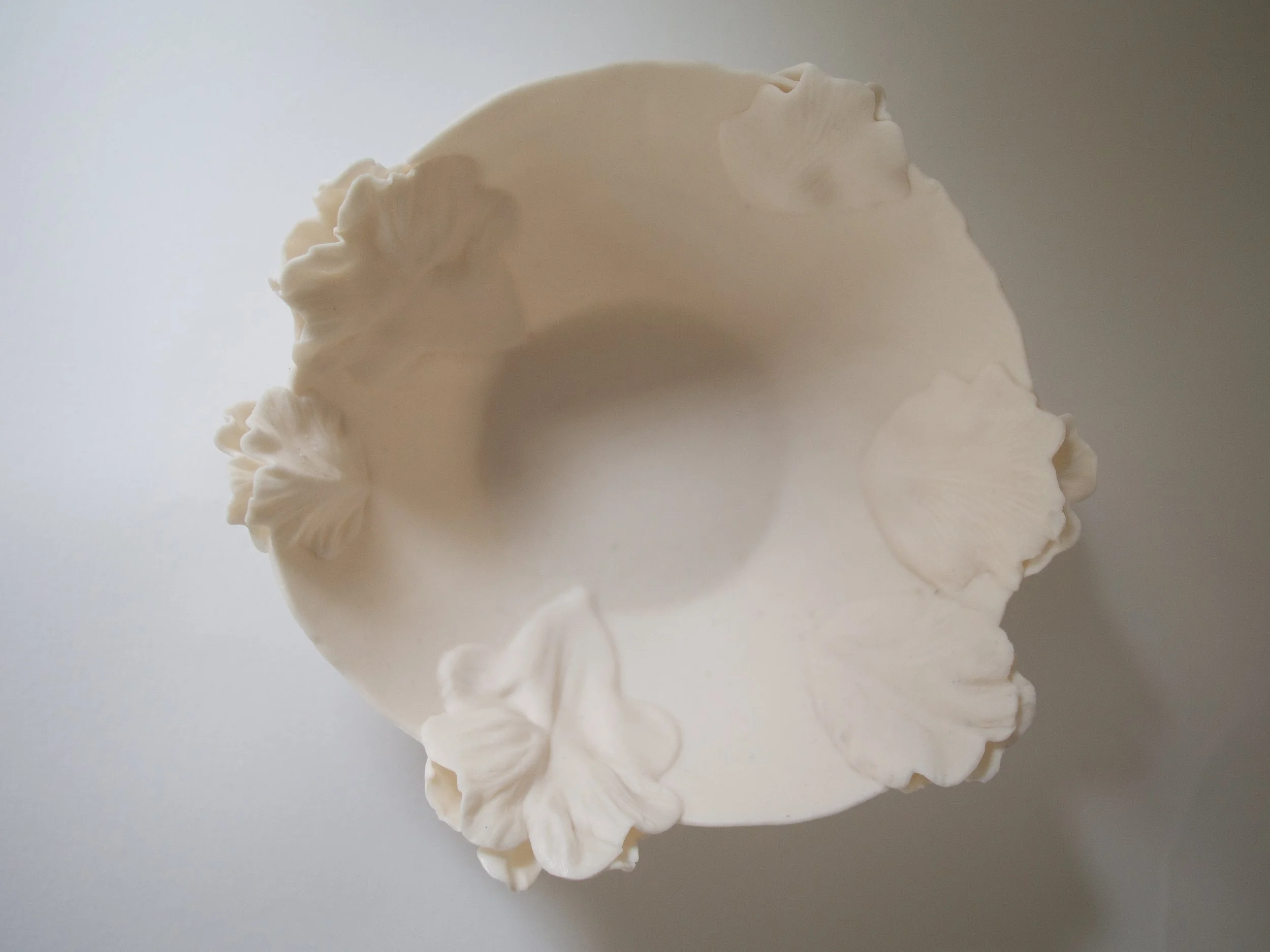 A white ceramic or porcelain vase with decorative floral or leaf patterns around its rim, viewed from above against a light background.