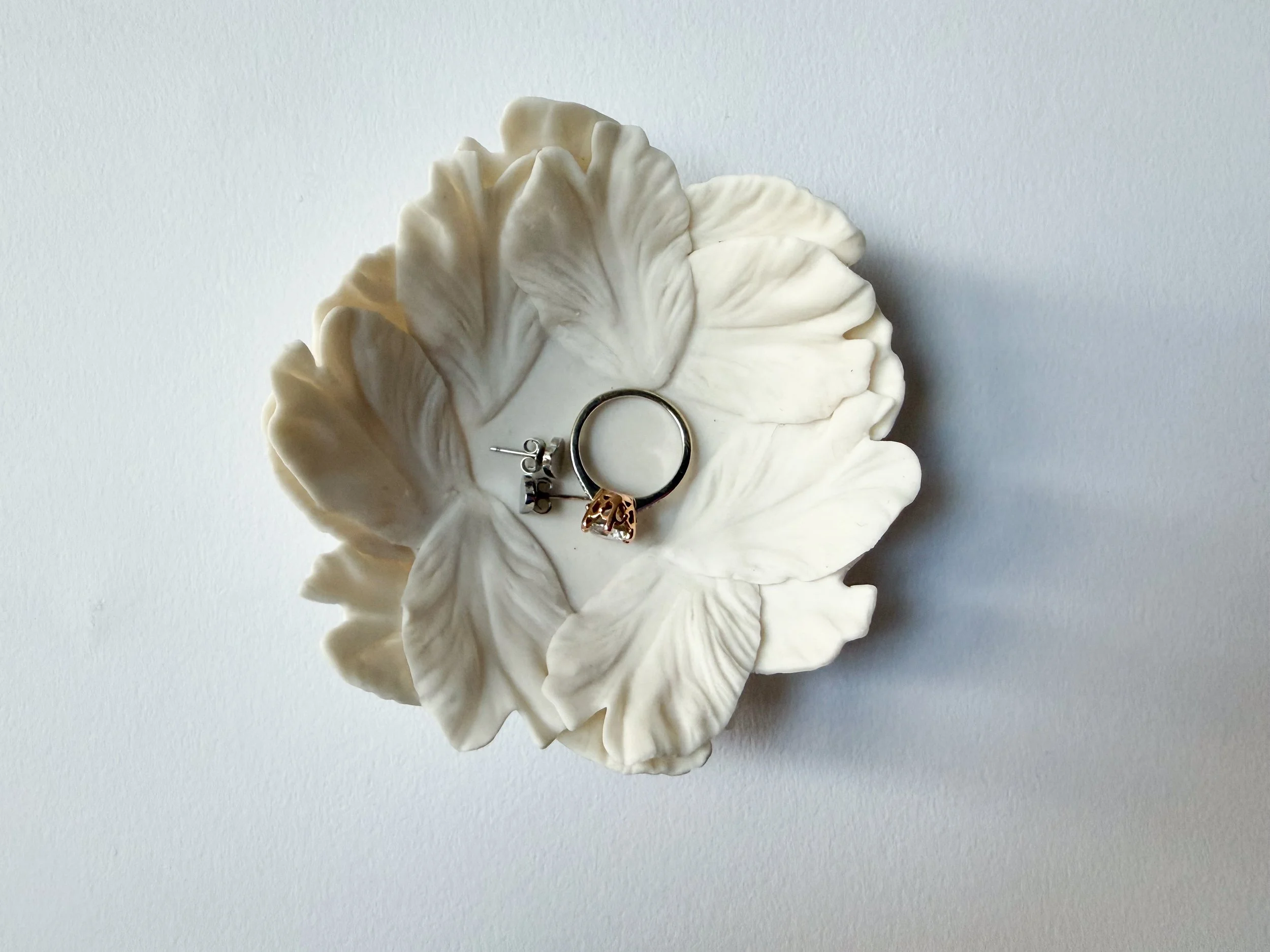Porcelain White flower-shaped dish holding a silver ring with a gold skull charm and a small silver earring.