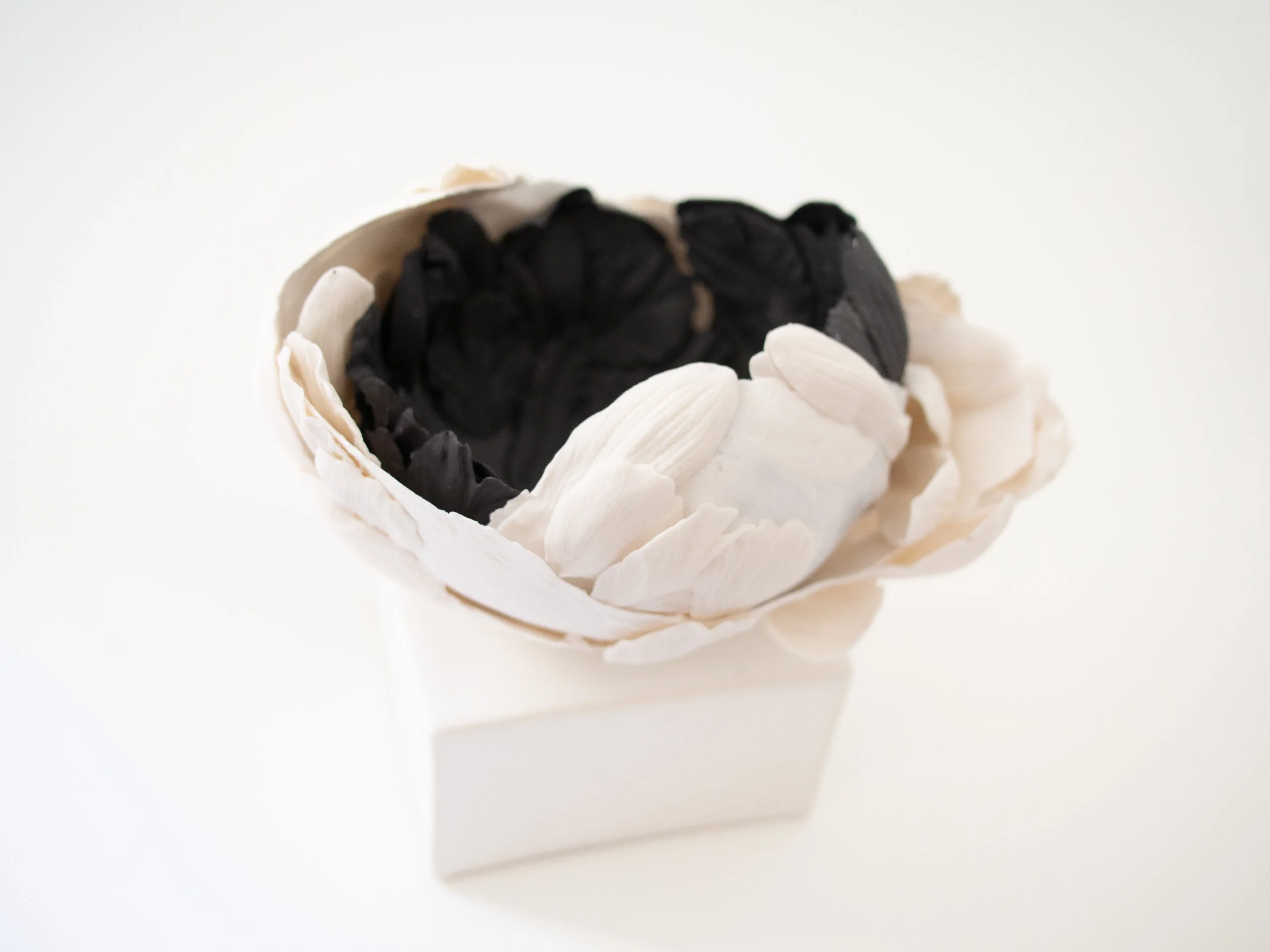 A white ceramic bowl filled with black and white flower-shaped objects, arranged in an aesthetic pattern.