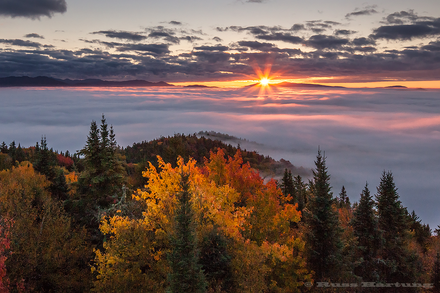 The first rays of the sun skip across the fog to spotlight the foreground trees on Goodnow Mountain. 