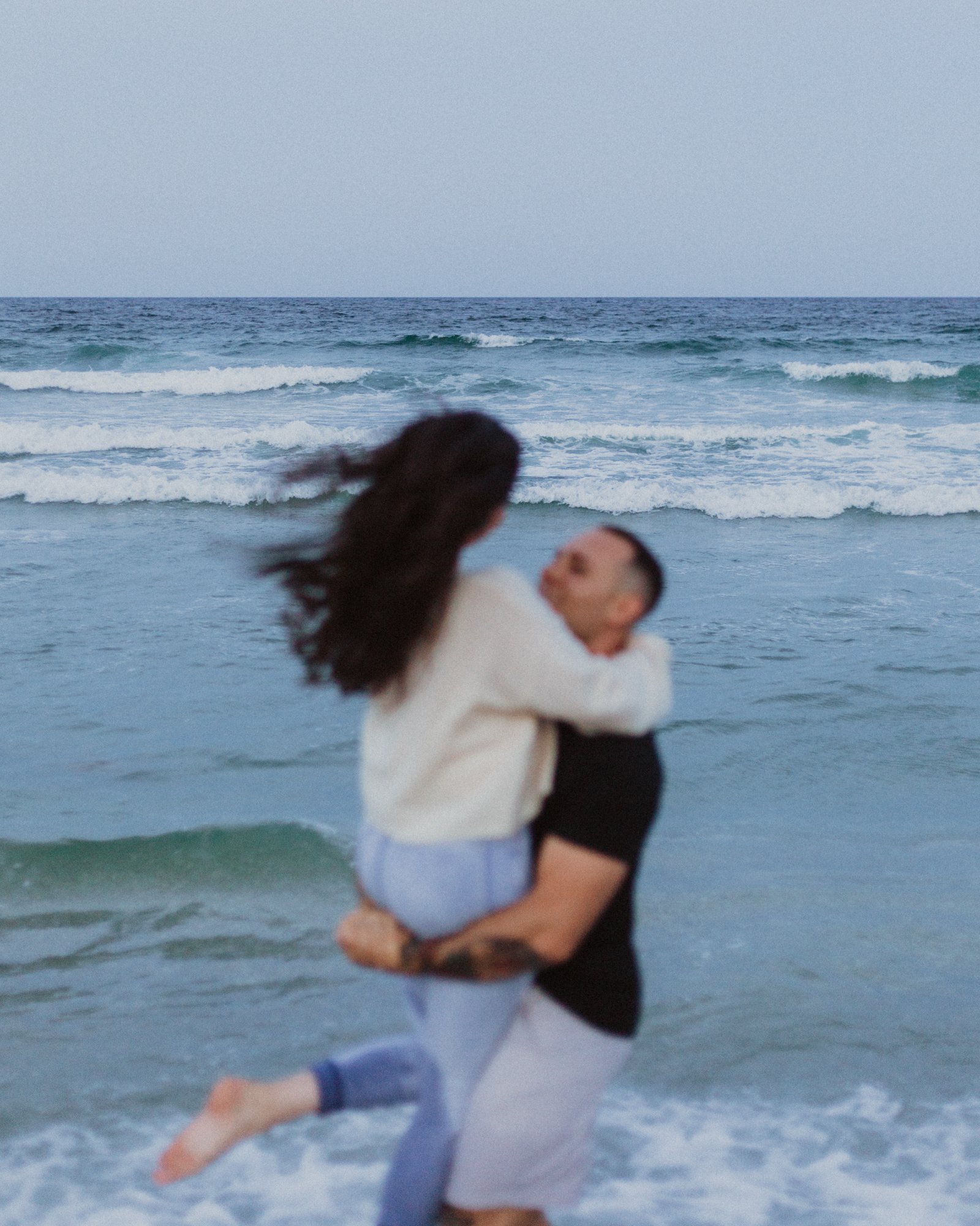 Creatively out of focus woman jumping into man's arms on the beach with ocean backdrop at the Jersey shore.