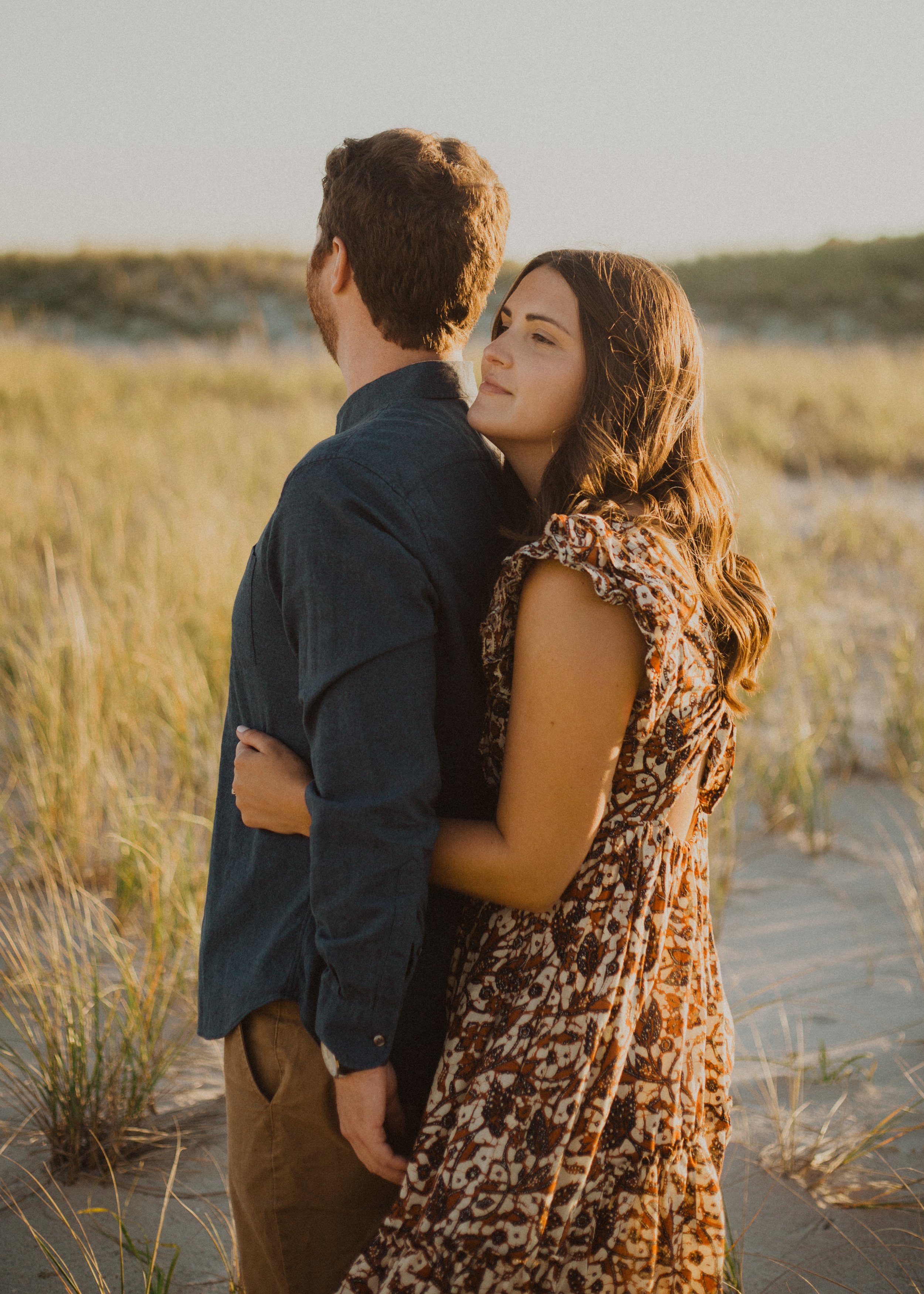 Thoughtful woman holding husband from behind while standing in sand dunes.