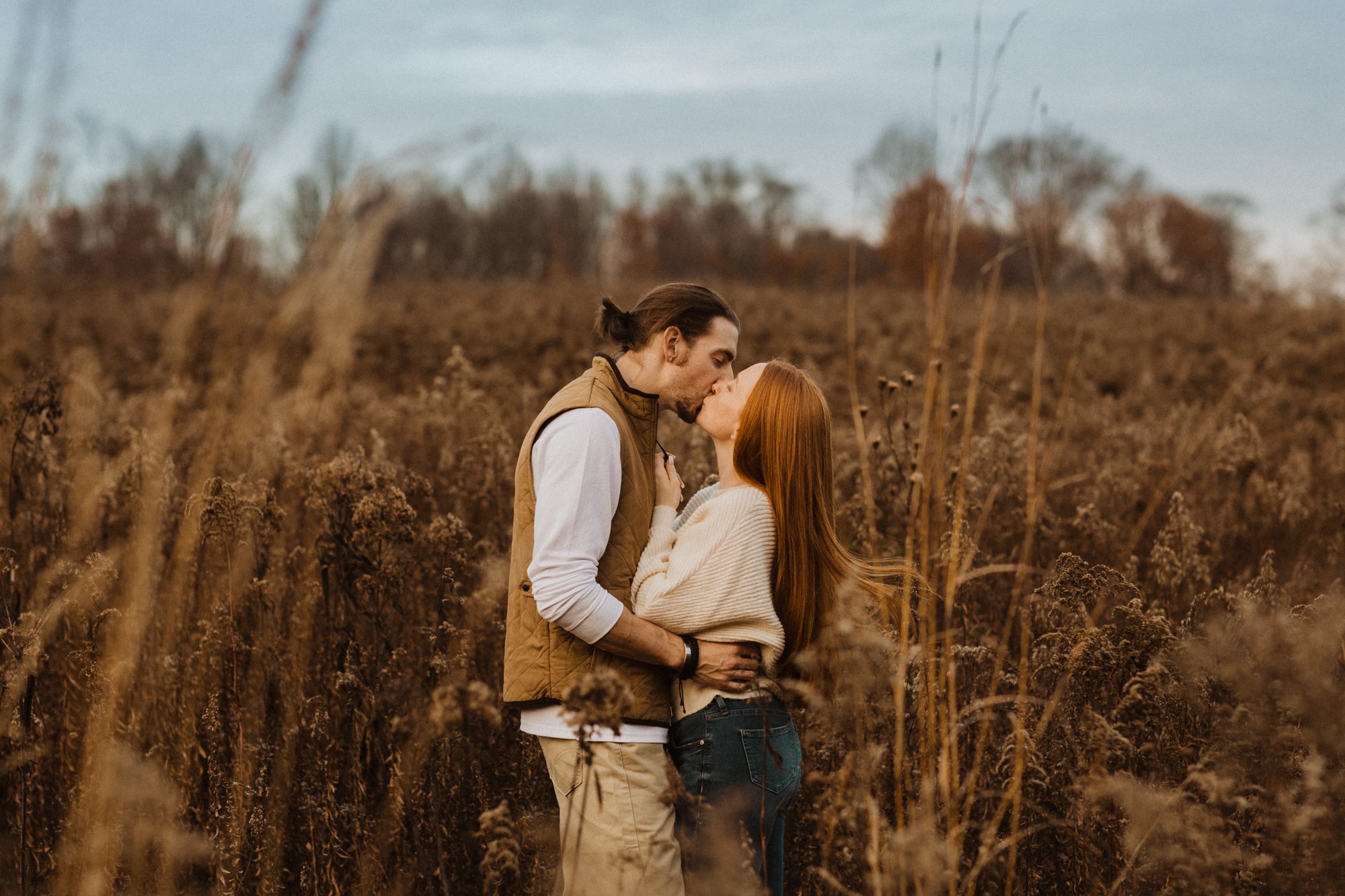 Man and woman kissing in a field of wheat during golden hour.