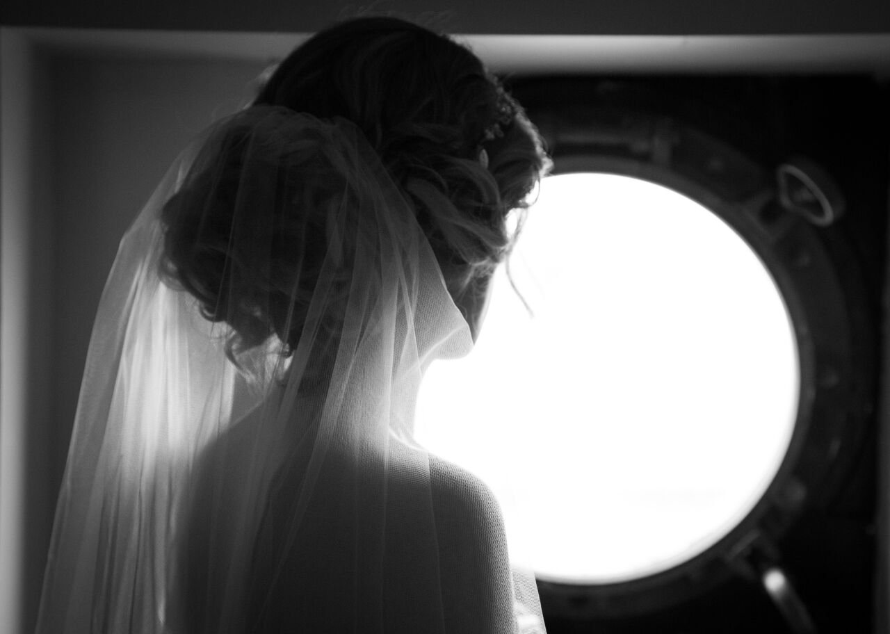 Bride wearing wedding veil, silhouette on circle porthole window in black and white.