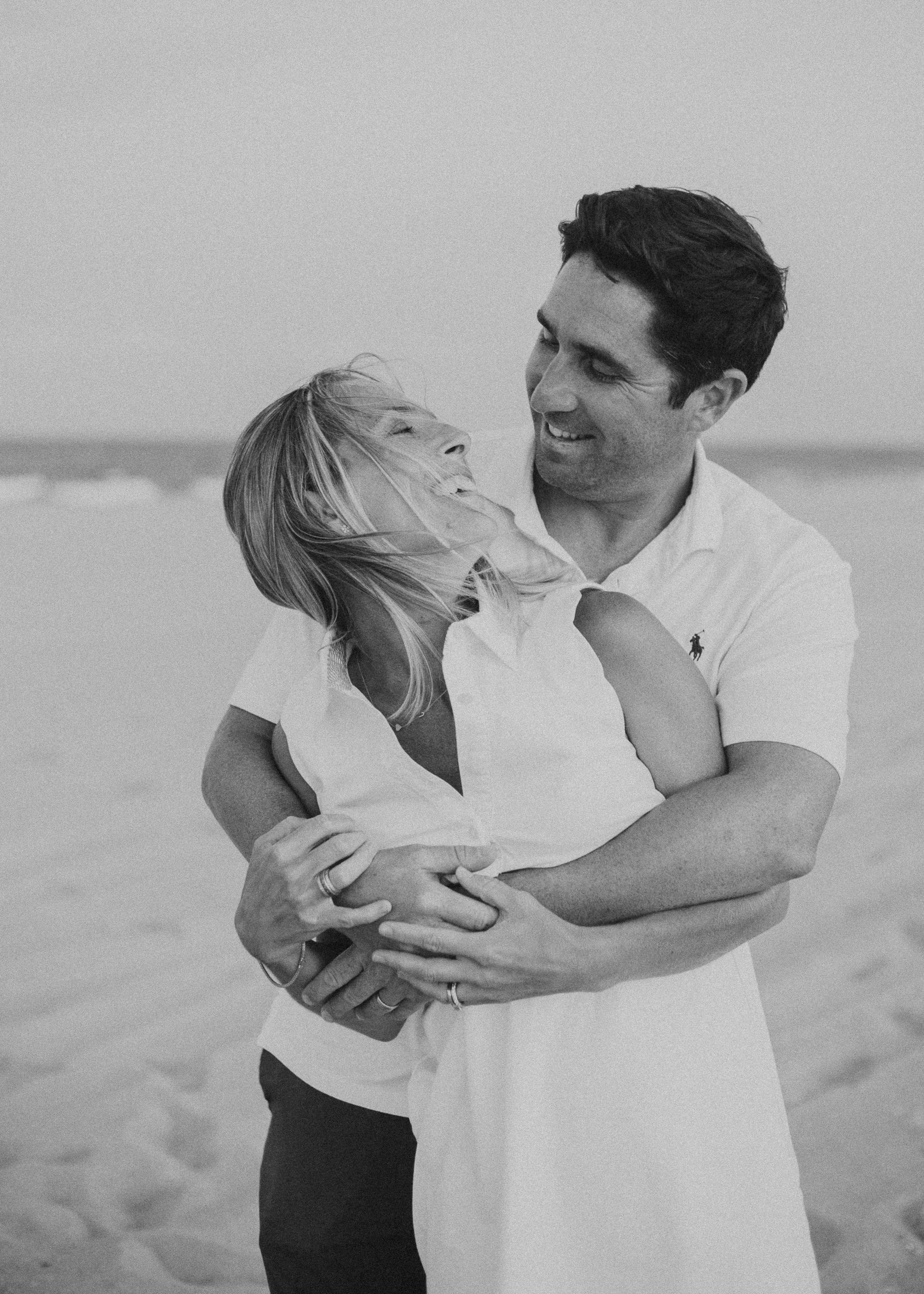 Man embracing woman from behind as she looks back at him and smiles. In black and white.