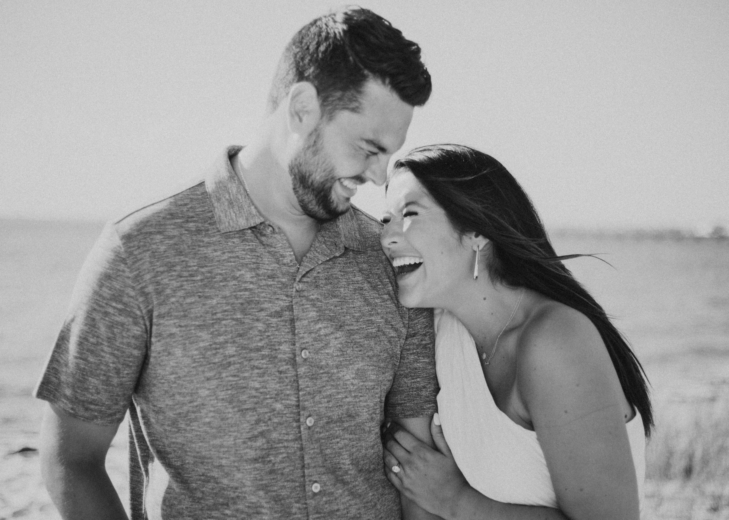 Candid moment of woman laughing on partner's shoulder taken during immediately following marriage proposal.