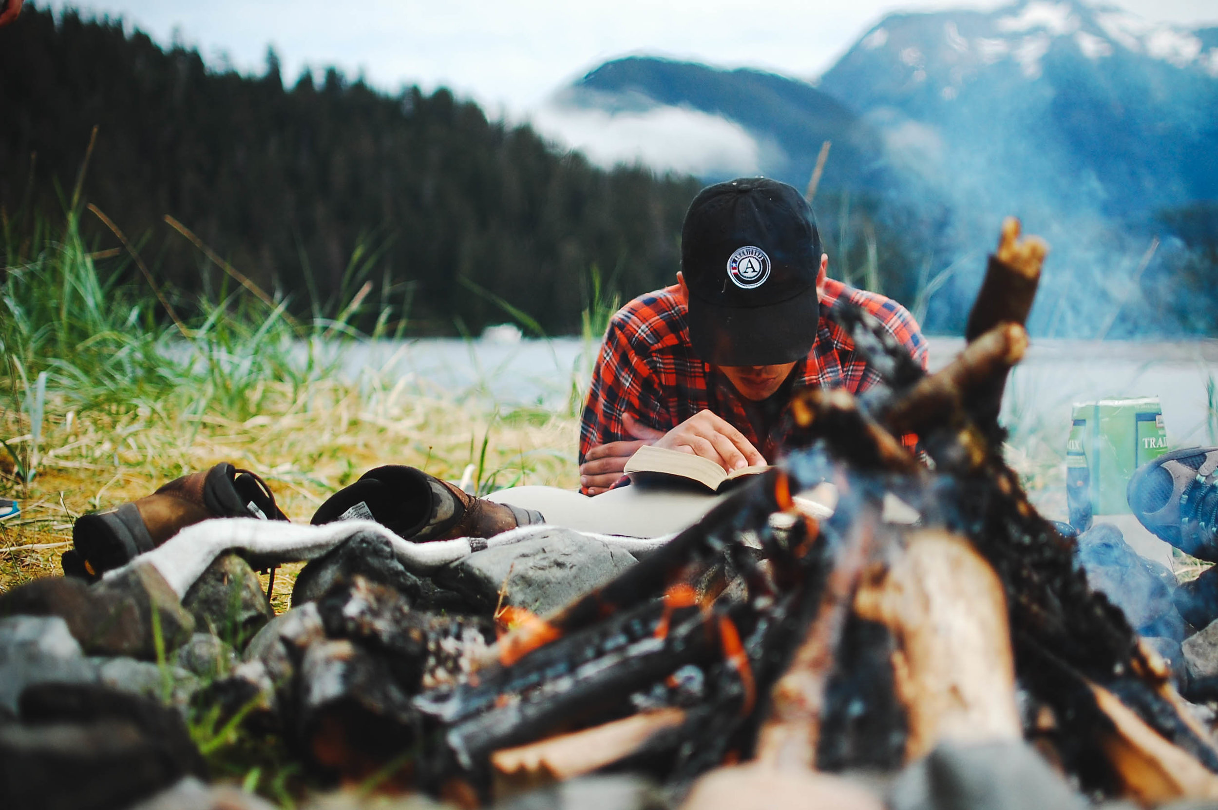N. dries his shoes and reads by the fire while camping in southeast Alaska