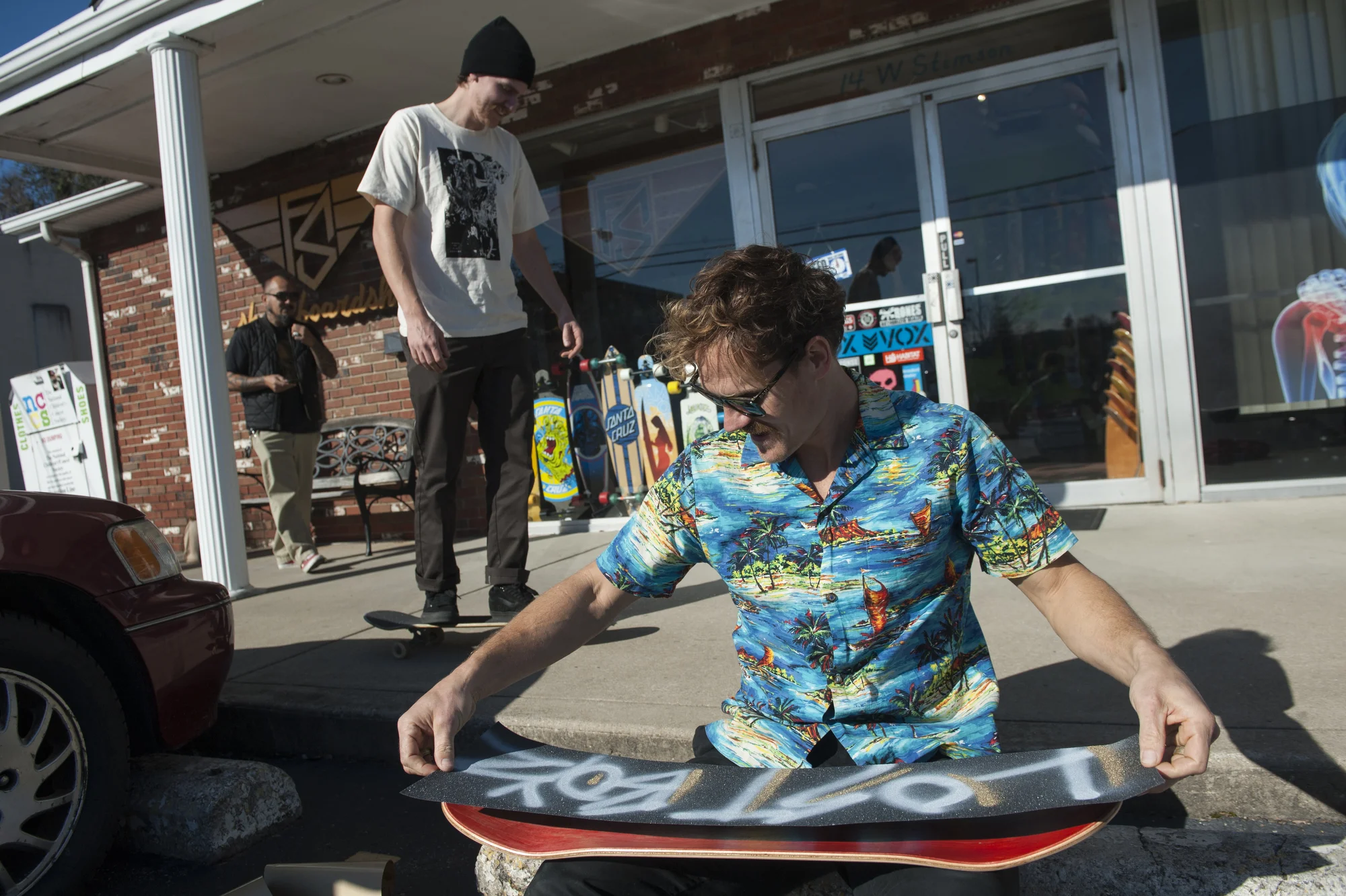 Moss Miller puts grip tape on a new board in front of his shop, Flipside, before heading out to skate around Athens. 