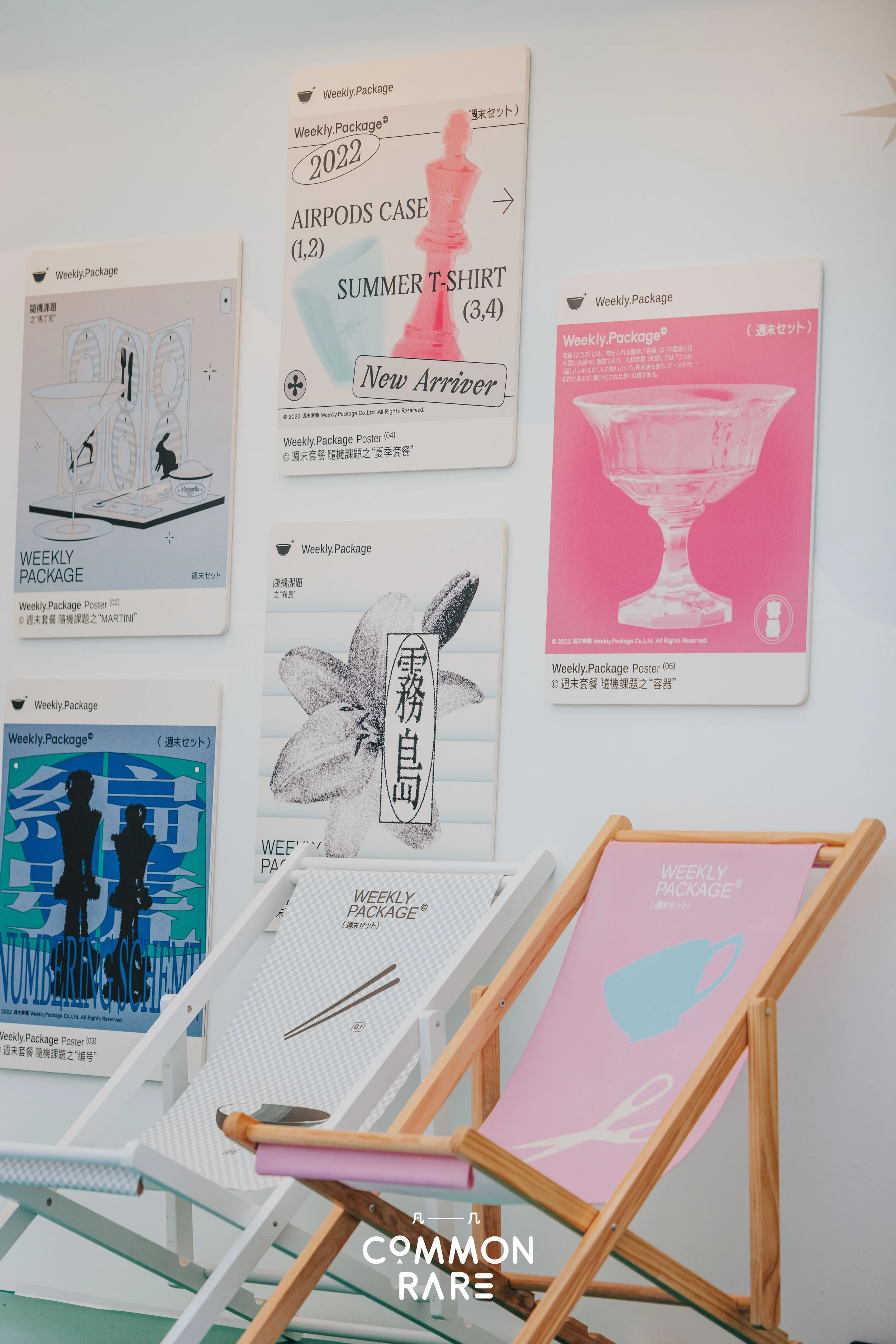 Display of several posters and deck chairs with various designs and text, including pink and white colors, on a wall.