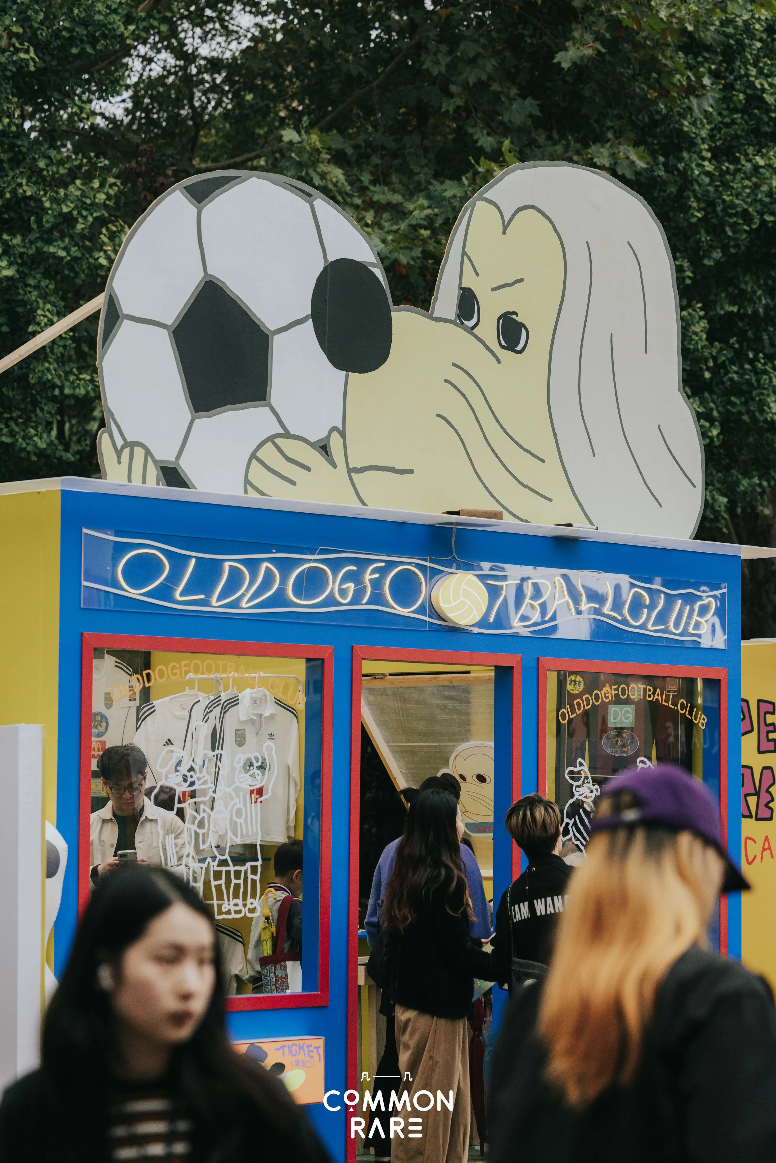 People gather around an Oregon Old Dog Football Club booth with a large cartoon dog and soccer ball illustration on top.