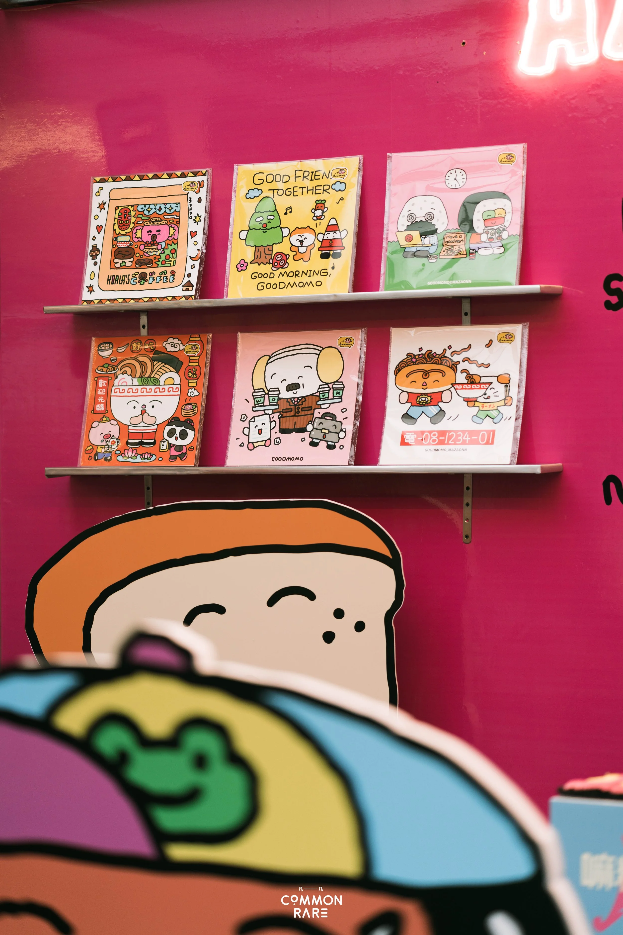 Colorful illustrated posters on a pink wall featuring cartoon characters and food, with a partial sign reading 'COMMON RARE' at the bottom.