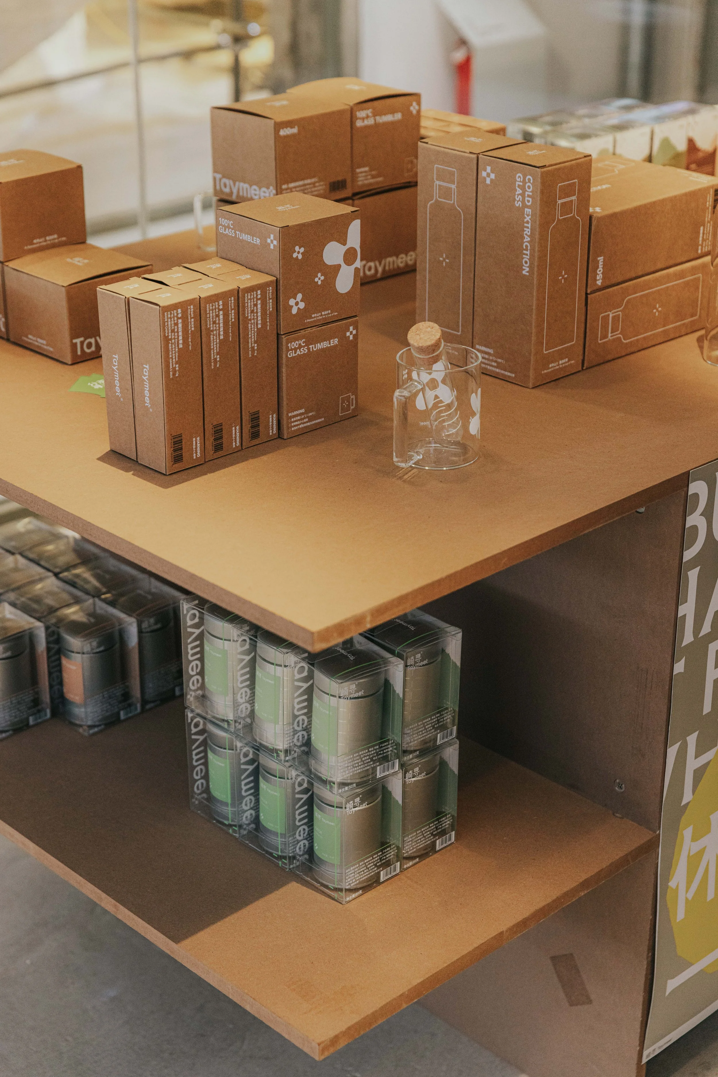 Display of glass tumblers and bottles with packaging on wooden shelves in a store.