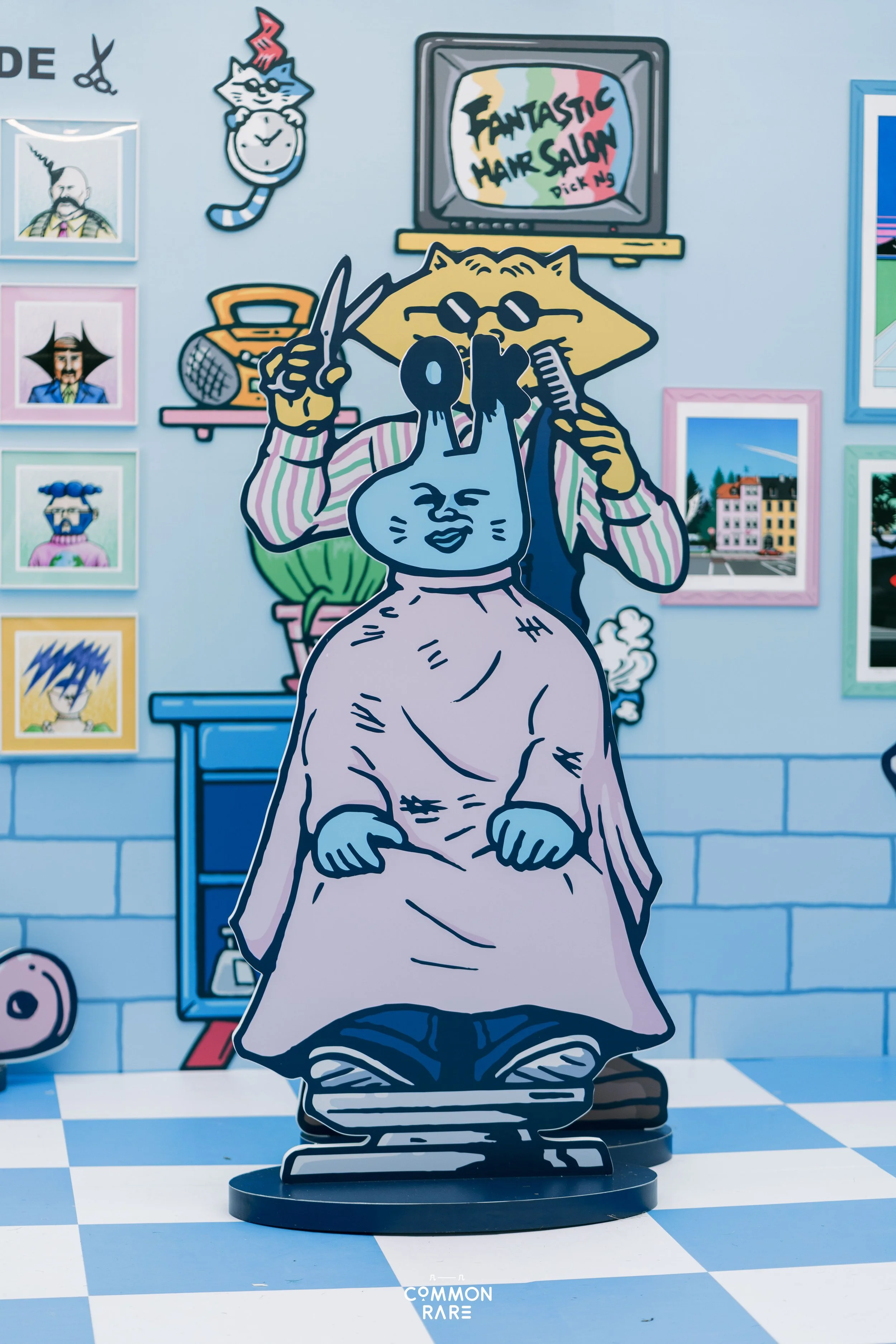 Colorful cartoon-style artwork featuring a cut-out of a cat with glasses, a woman with a cat face holding scissors and a comb, set against a background of framed pictures, a TV with art on the screen reading 'Fantastic Hair Salon,' and various decora
