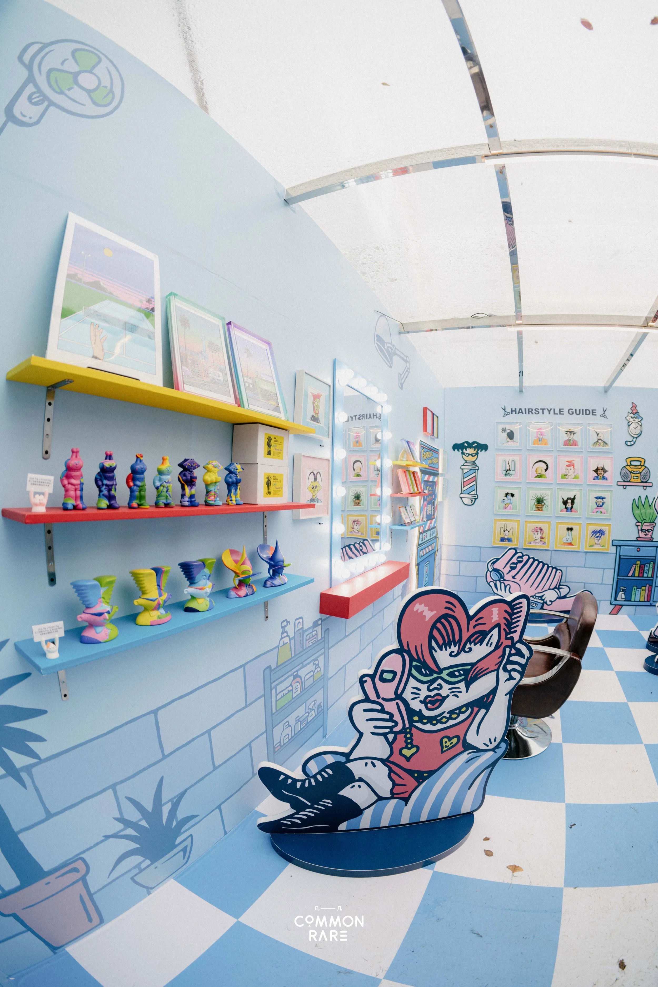 Colorful cartoon hair salon scene with a large illustration of a woman with red hair, sunglasses, and a phone sitting against a blue and white checkered floor and wall. Shelves display various colorful figurines and framed artwork, including a hair-t
