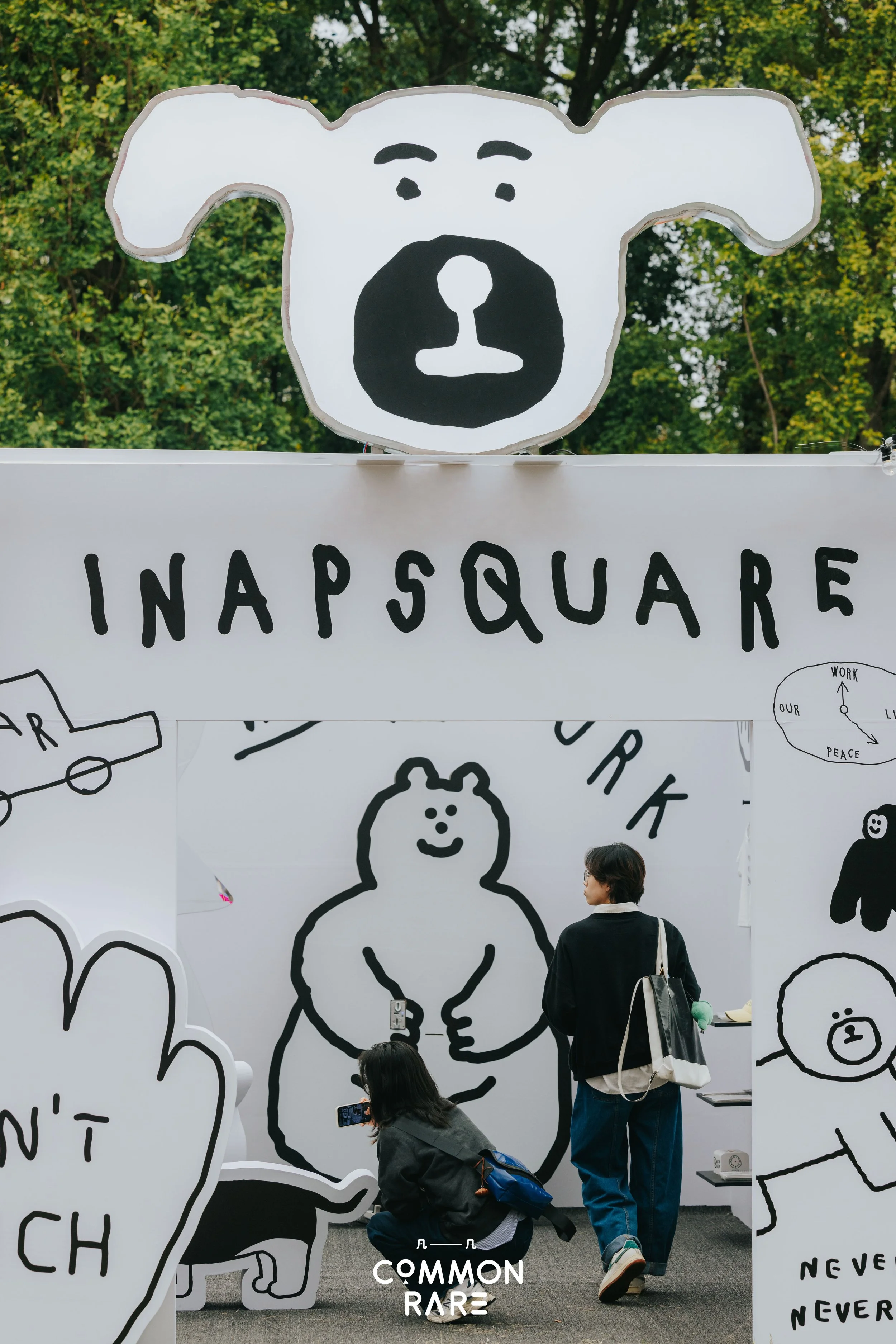 People taking photos at an art exhibition with black and white illustrations of a bear on the walls and sign reading 'INAPSQUARE'.