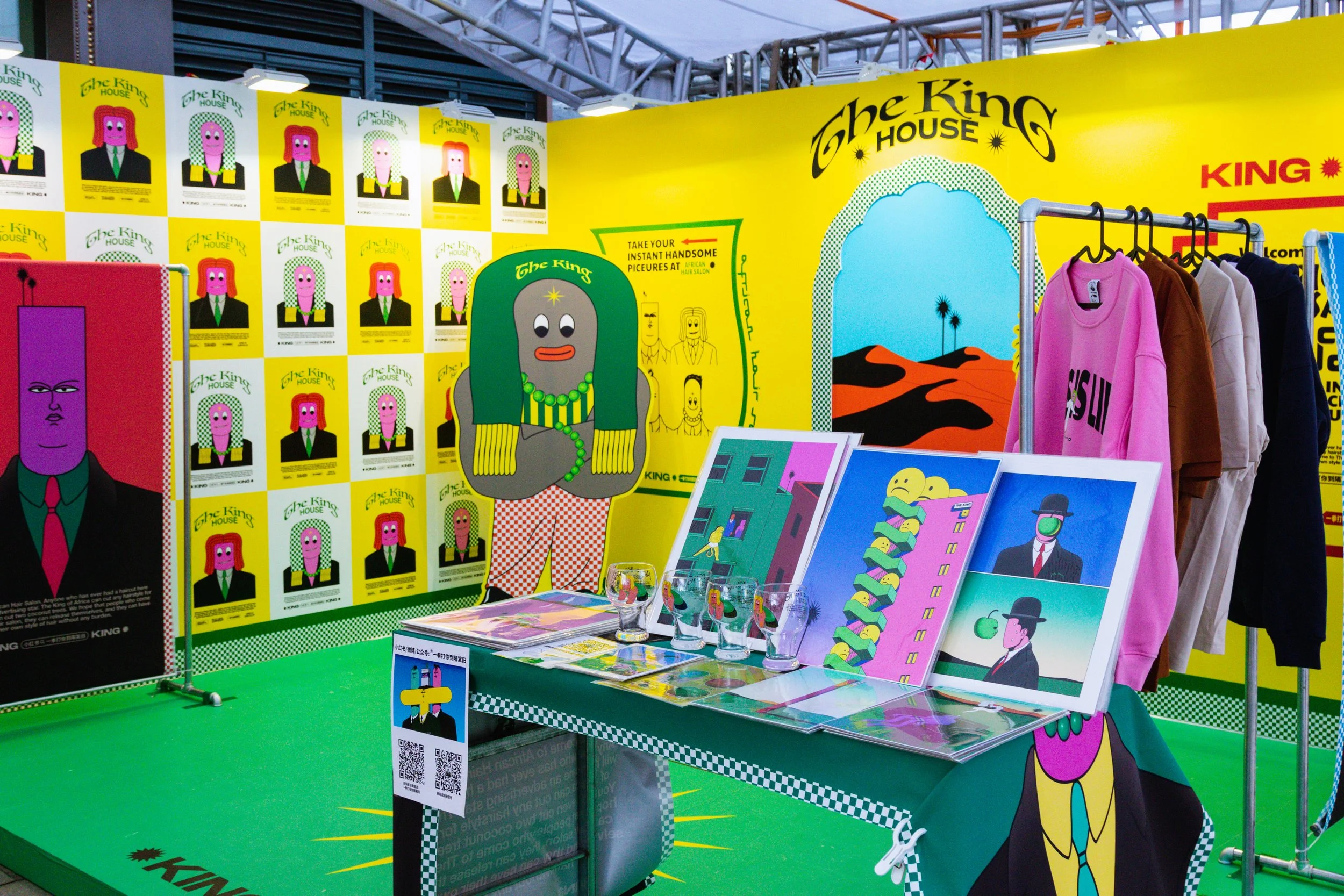 Display booth featuring colorful pop art posters and clothing items, with a bright yellow background and cartoon character illustrations promoting The King House branding.