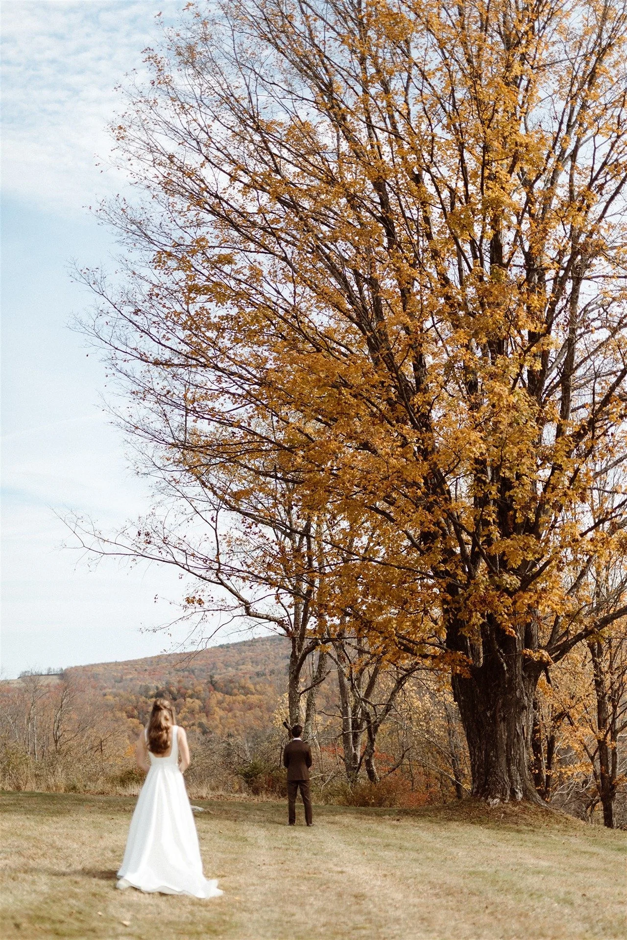 Autumn-Backdrop-First-Look-With-Bride-Walking-Up-To-Groom-And-Grooms-Back-Turned-To-Her