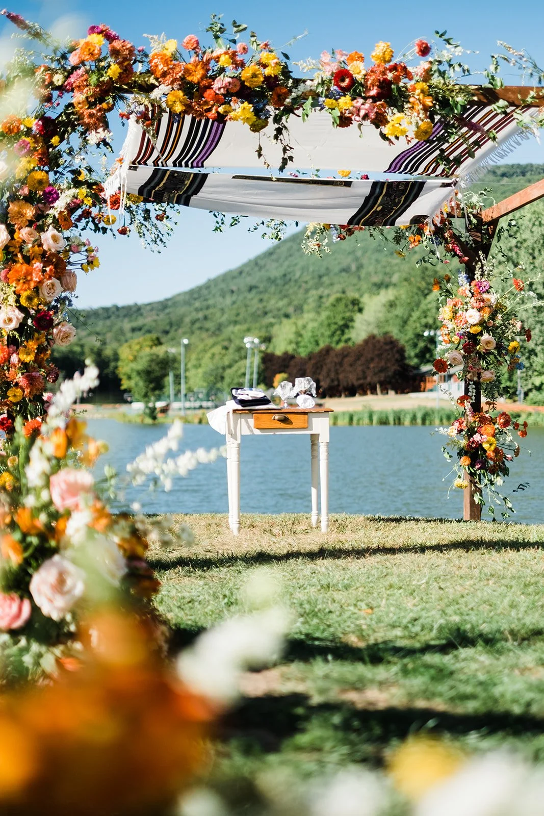 outdoor-ceremony-at-camp-timberlake-white-vintage-table-under-chuppah-vibrant-florals.jpg