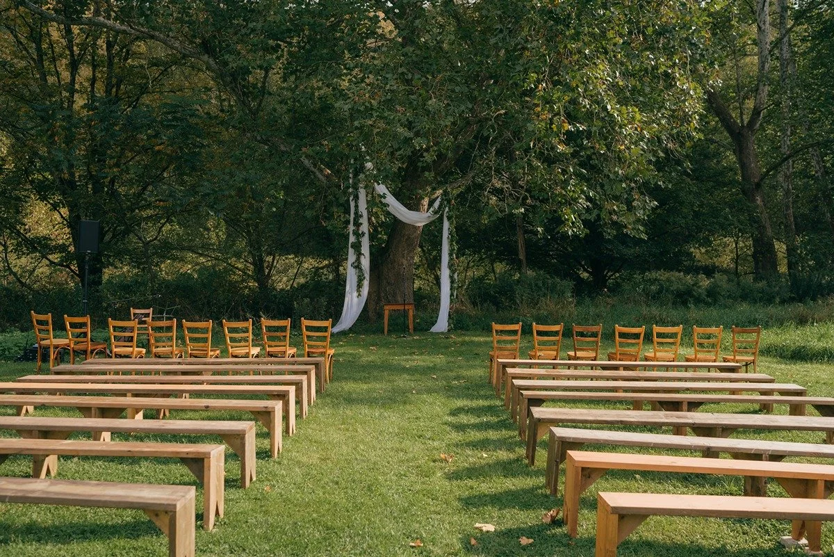 outdoor-hudson-valley-ceremony-fabric-in-tree-and-wooden-benches-wedding-planner-setup-landscape-photo.jpg