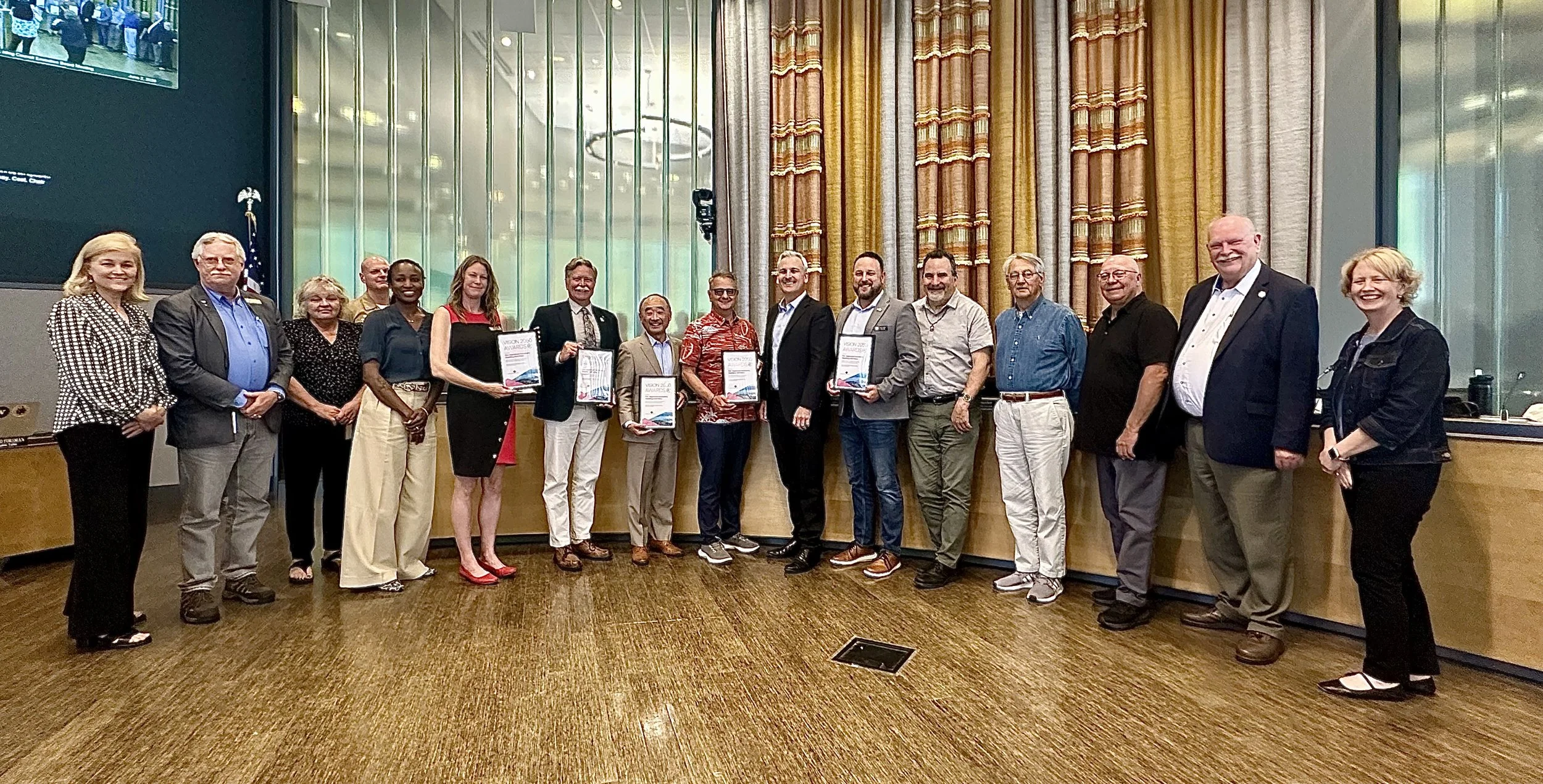 Board members stand in front of a dais holding award certificates