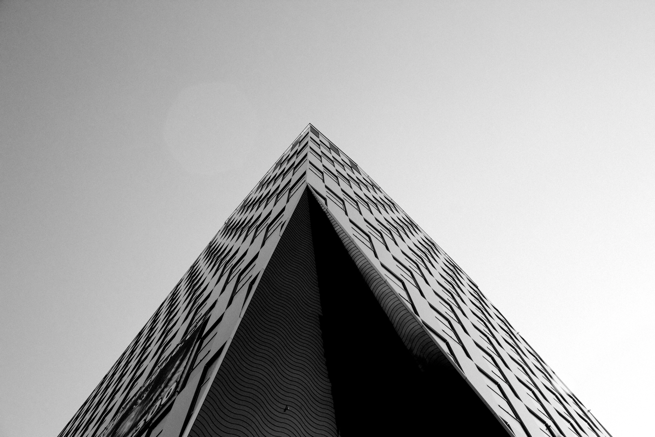Low-angle black-and-white photo of a modern skyscraper with a pointed tip, featuring a pattern of windows, against a clear sky.