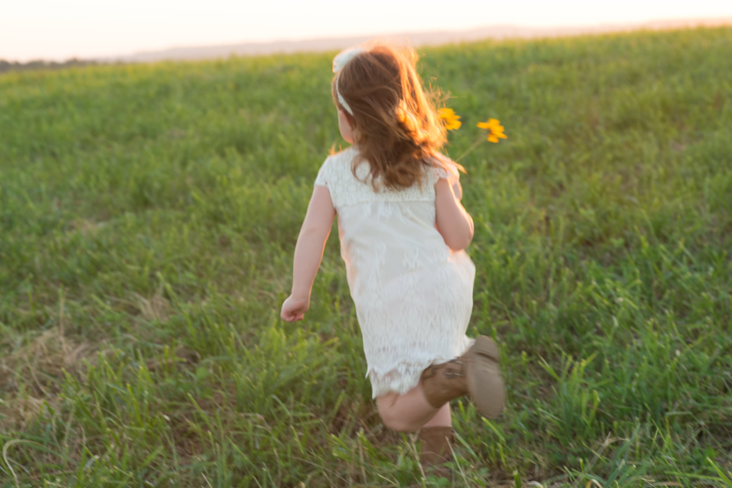 little girl running with a flower in a meadow at sunset