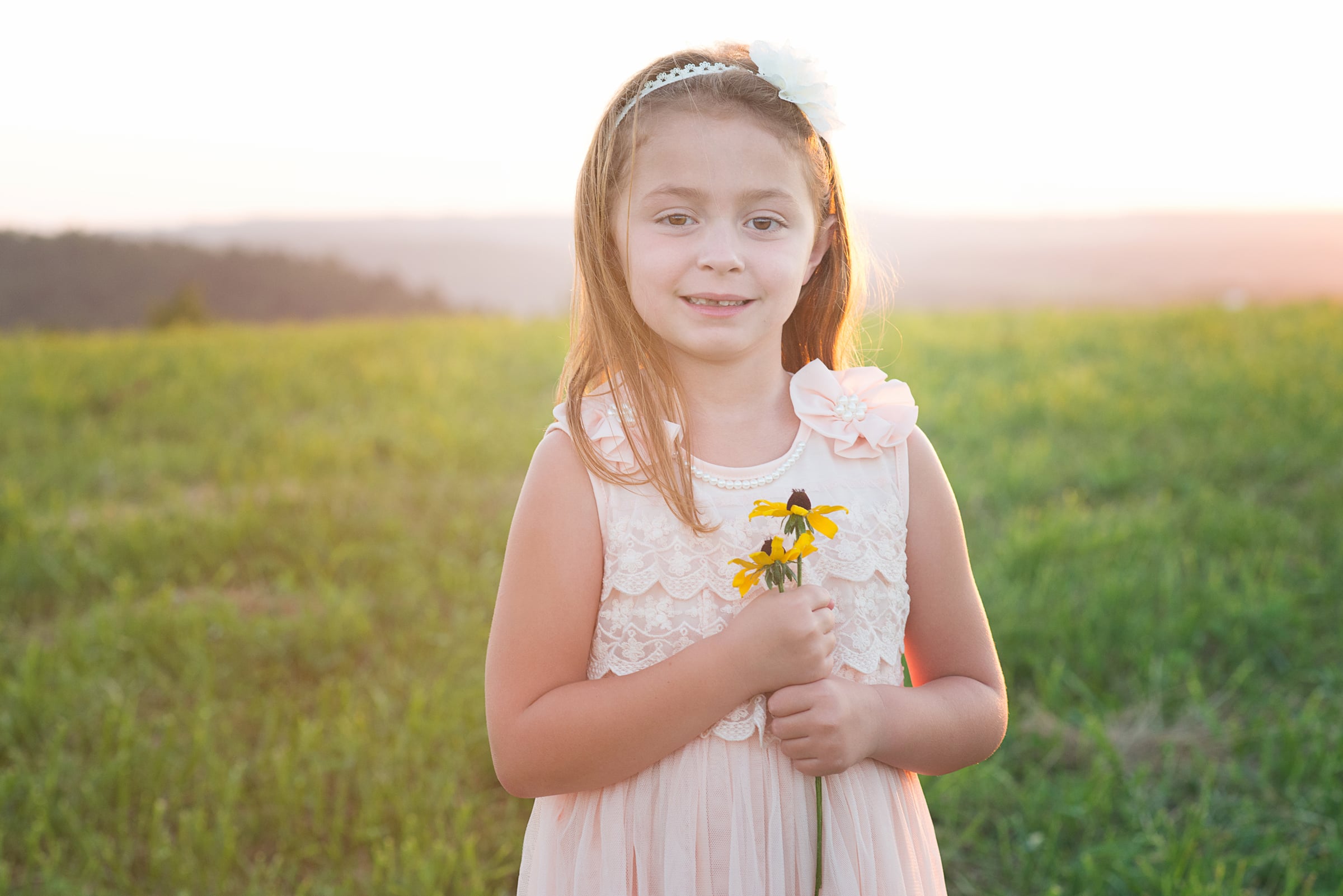 little girl holds a flower at sunset