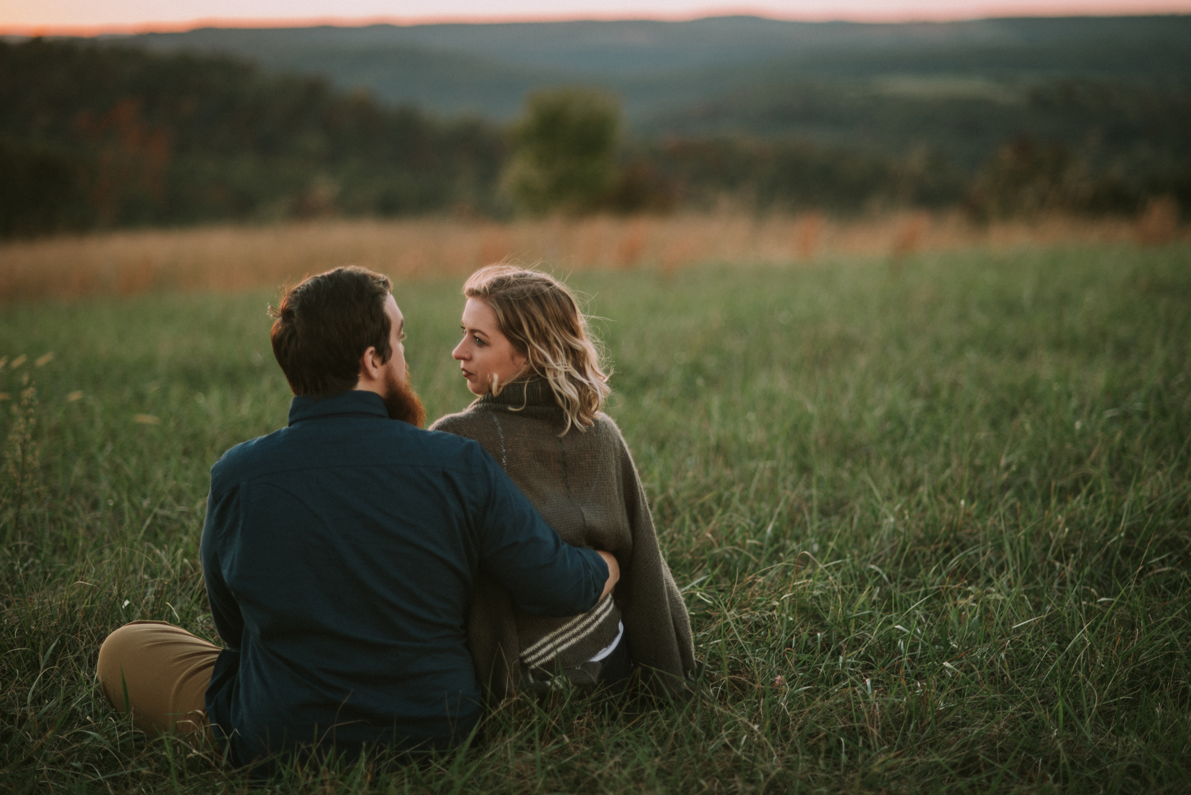 Couple sits in a meadow at sunset