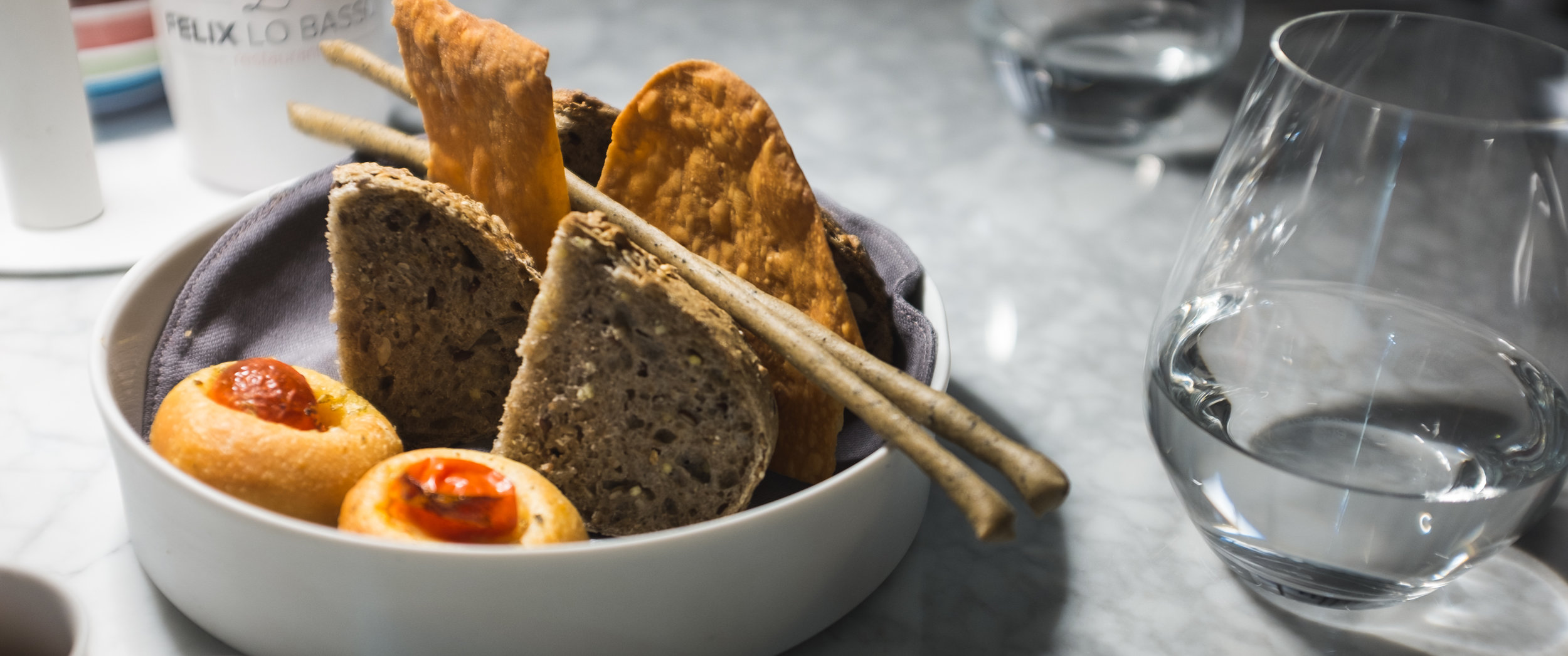 Felix Lo Basso. Duona su grūdais ir sėkloimis, grissini, focaccia su pomidorais ir svogūnų traškučiai. Felix Lo Basso. Bread with grains and seeds, grissini, tomato focaccia and onion chips.