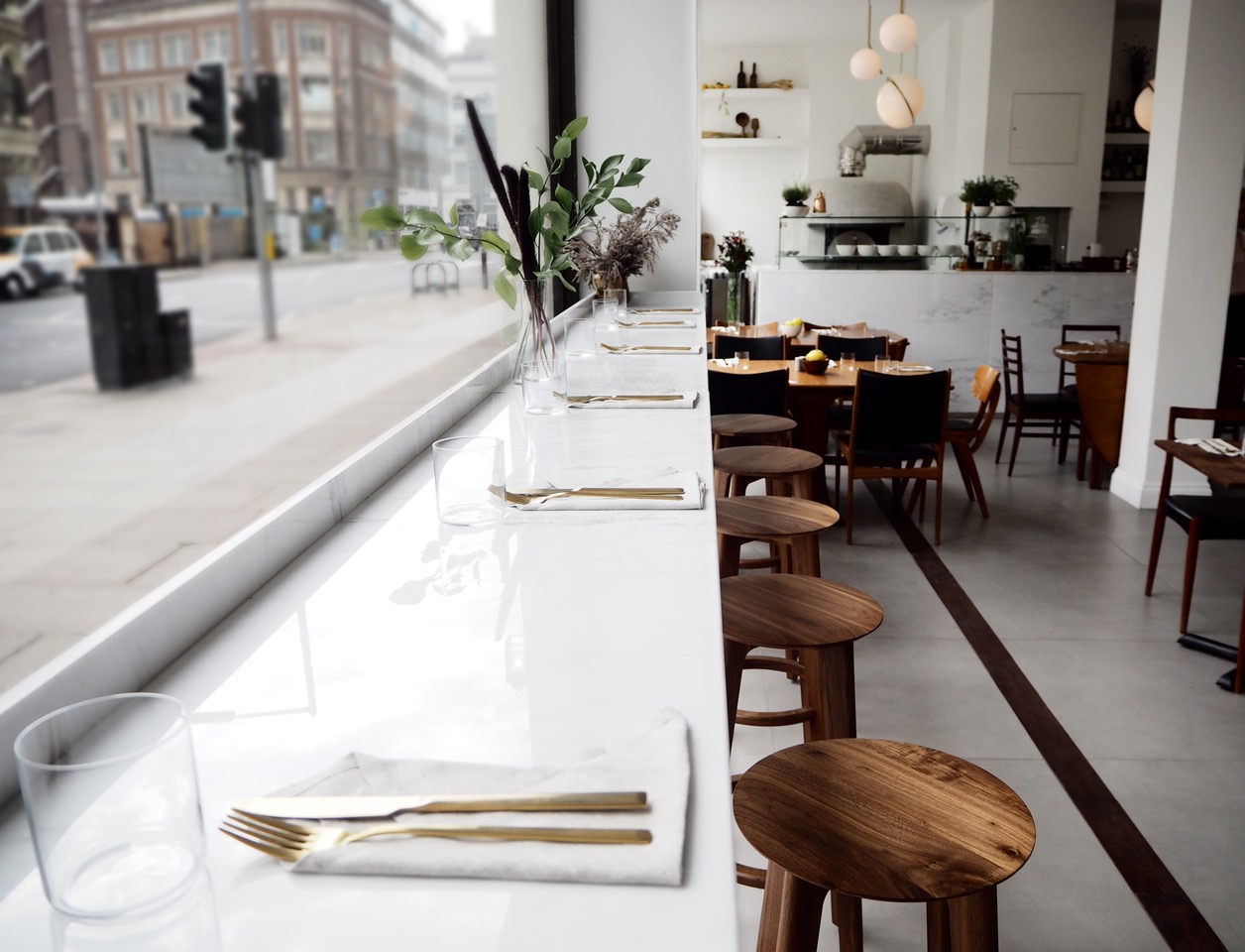With the influence of Naples, the land where lemons grow, 'Over opens in the art district of the British capital. 'Over is a traditional Neapolitan cuisine restaurant with an innovative contemporary twist. Inspired by the beauty and harmony of an artistic space, Quiet Studios creates for 'Over a serene, pure and bright space, with the combination of noble materials such as marble, ceramic, brass and walnut. The chosen furniture is teak Scandinavian-style from mid-twentieth century, carefully selected from various antique dealers in London. Designed by Michael Anastassiades, the spherical lamps with gold brackets combine with household goods and decorative details. Quiet Studios creates a harmonious table composition through a selection of Scandinavian ceramics, wood vases from Japan, household goods of Portuguese craftsmanship, unique chandeliers and antique pieces acquired in Berlin and London antiquaries. In addition to the purchased products, Quiet Studios designs unique pieces for 'Over, which provide identity and uniqueness to the brand, as the design of leather pieces produced by hand in southern Spain. 'Over represents the union of the classic and minimalist in a harmonious and distinguished space, amid the bustle of London.