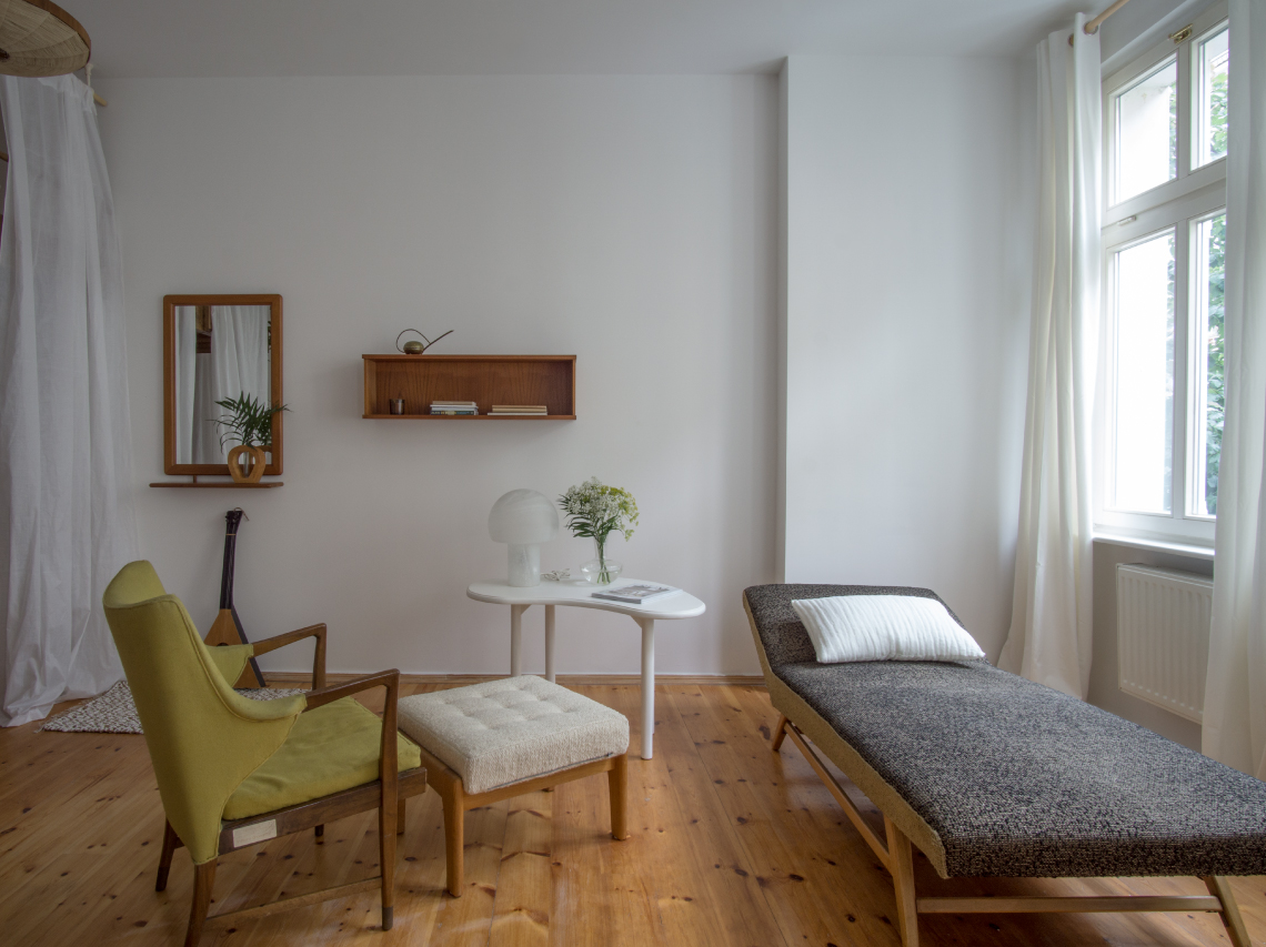 The Mauerpark Studio is a residence in the dynamic German capital, intended as a temporary rental property. The design concept balances homeliness, comfort and design for medium to long term guests and residents accordingly. The studio’s design makes the most of vertical space given by the apartment’s high ceilings. A wood custom made ‘Hochbett’, German high bed, creates a cosy sleeping area without detracting from the spaciousness of the main room, and soft white curtains give the option of a more private separation of the living area. The kitchen is made to measure. Light wood-fronted cabinets and open shelves are fitted into the space for storage, lined with crockery and hanging utensils. A dining space with rustic mismatched chairs is located next to the large window, filling the studio kitchen with bright daylight year-round. Having worked with experienced carpenters on the bespoke elements of the project, wood features as the key material and design texture throughout, giving a handcrafted feel to custom-made pieces. For Quiet Studios, the essence of this craft plays a fundamental role in creating the feeling of home. Modern midcentury style antique furniture sourced from local Berlin dealers are accompanied by small decorative features such as basket lamps, solid teak mirrors and vintage timepieces. A trademark Quiet Studios touch of greenery adds natural vigour and life to the bright space.