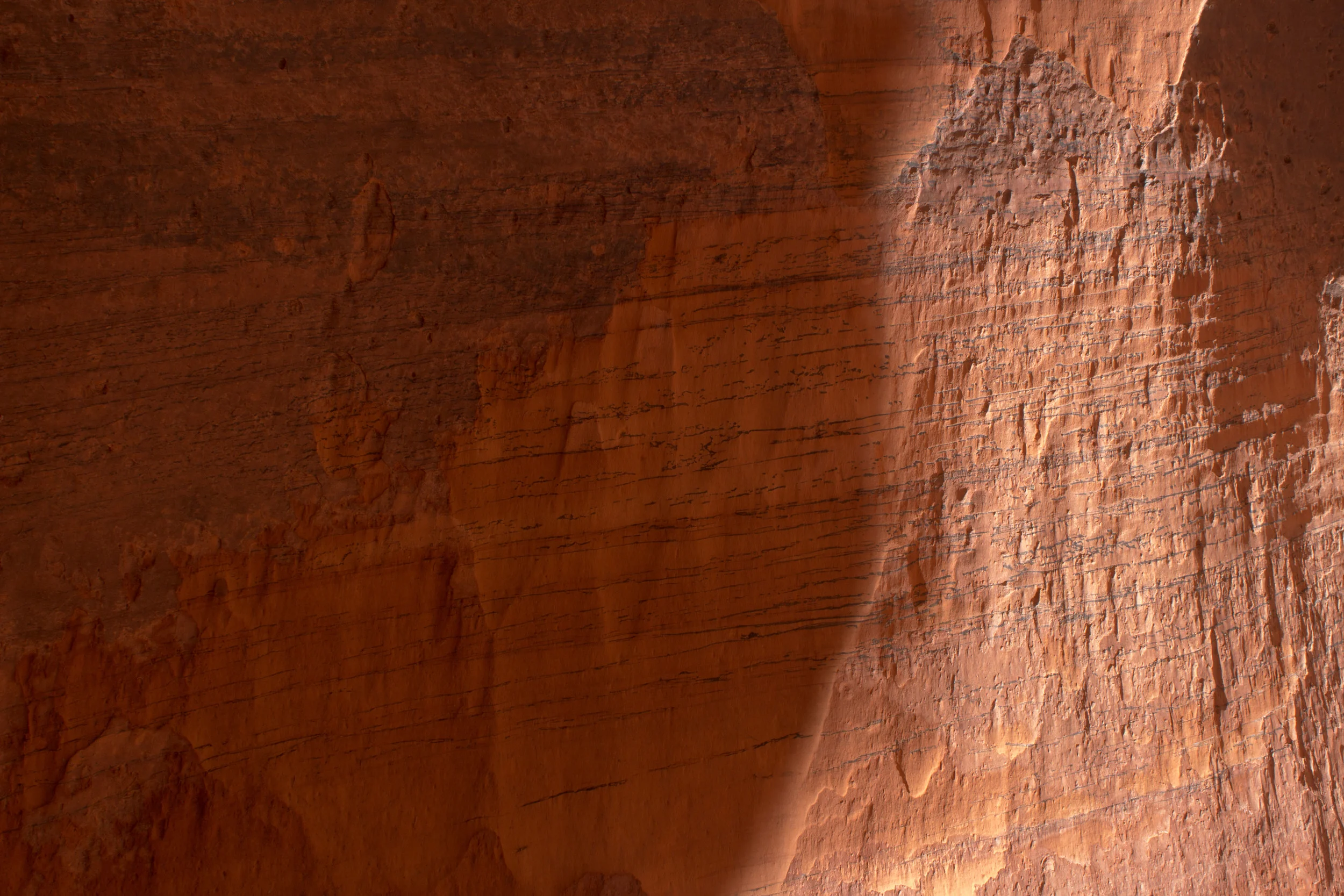  An orange slot canyon with diagonal streaks across the rock. The right third is a brighter orange with sun shining on it. 