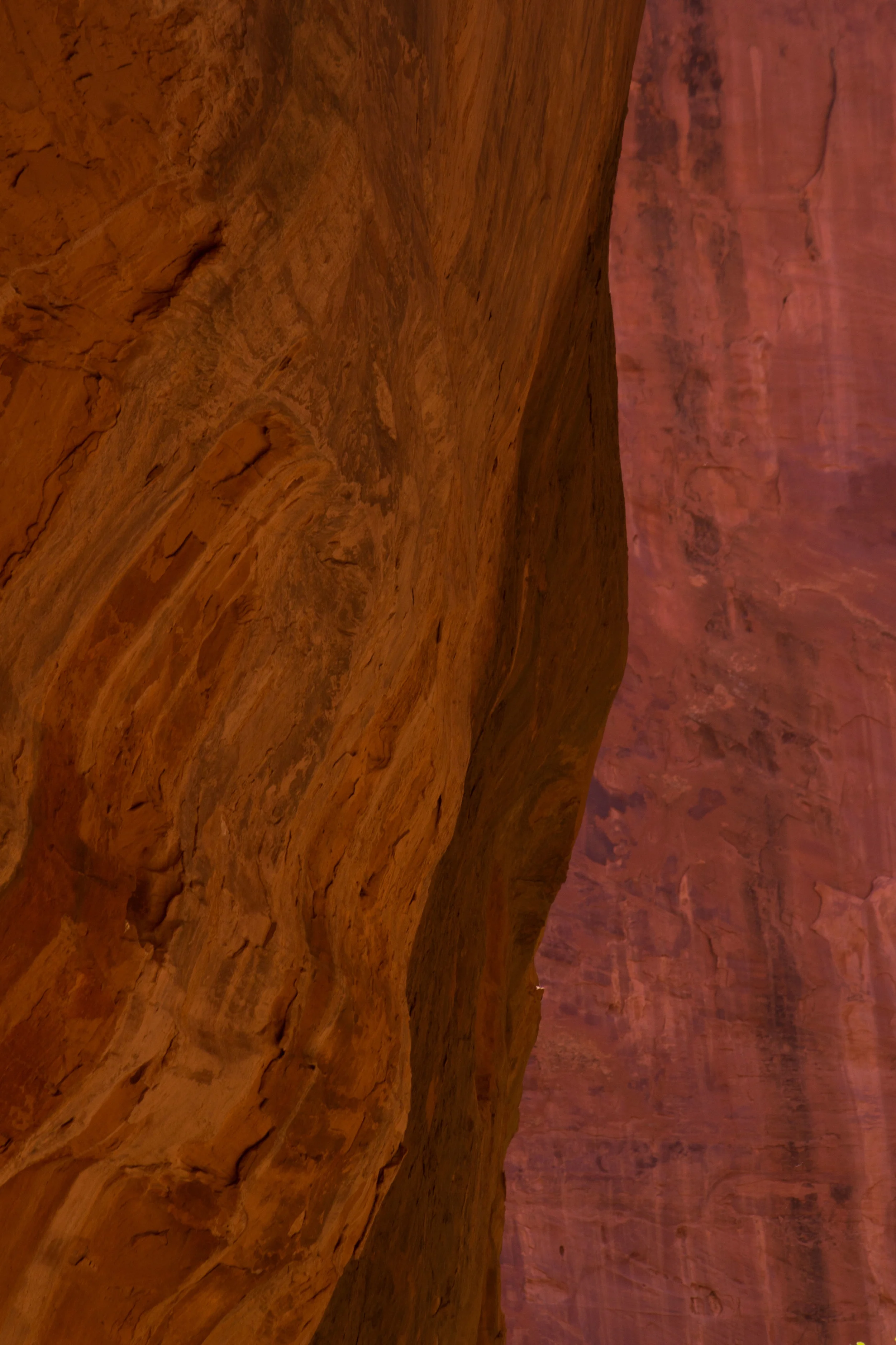  A photo of a slot canyon with orange brown on the left side and reddish brown on the right. They appear to be like curtains made of stone. 