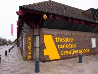 Image shows the side of the Albany, our 2018 venue. It is a brown, one story brick building with yellow lettering. Image Credit: The Albany, © Marianne Chua
