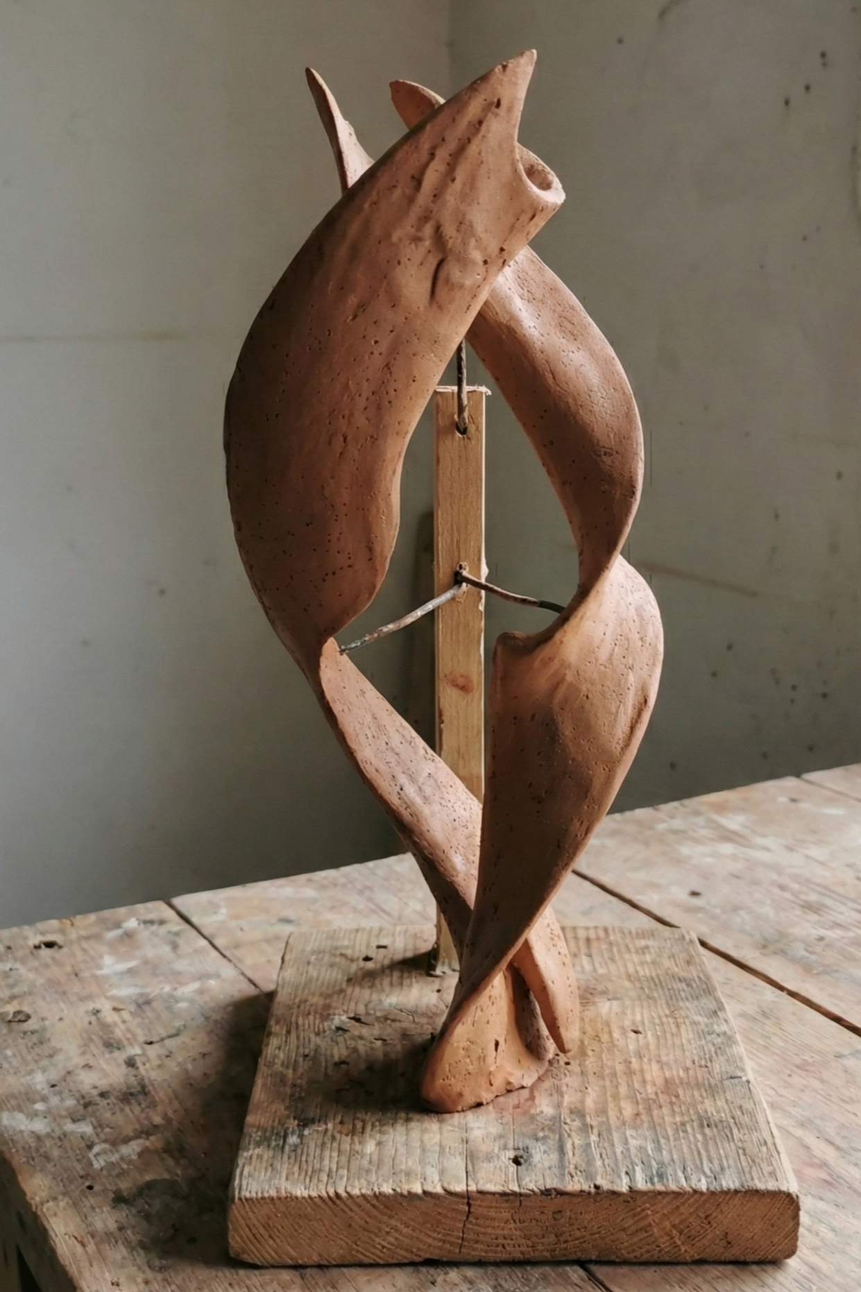 Abstract wooden sculpture mounted on a wooden base, displayed on a wooden surface.