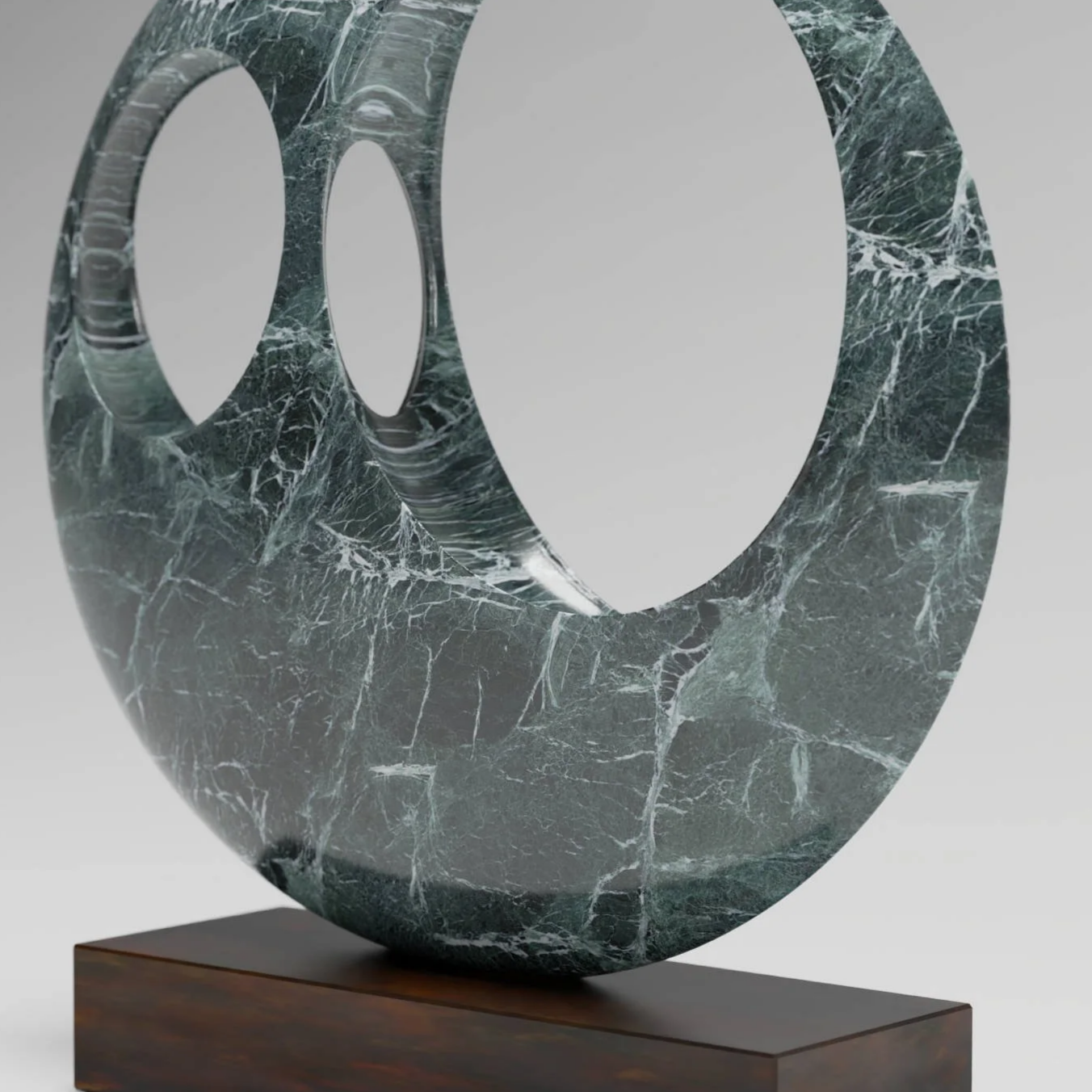 A modern sculpture made of green marble with white veins, shaped like a large, stylized letter 'a' or similar abstract form, mounted on a wooden base.