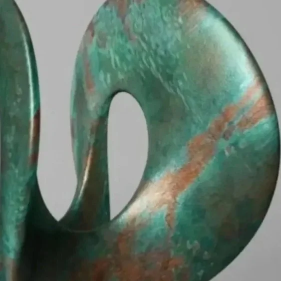 Abstract sculpture with a smooth, twisted, donut shape made of green and rust-colored metal, mounted on a gray stone base.