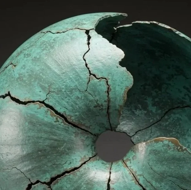 A large, turquoise-colored ceramic or stone sculpture with cracks, shaped like a donut or torus with a hollow center, mounted on a rectangular pedestal.